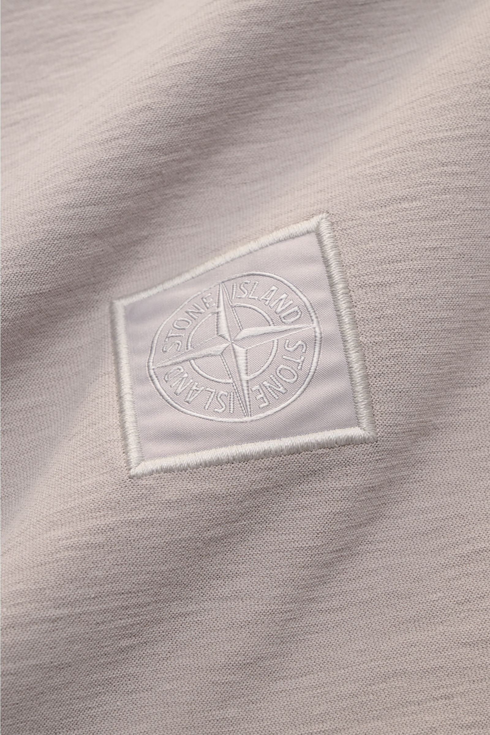 Nahaufnahme des tonalen STONE ISLAND-Kompasslogos auf dem Stone Island Longsleeve-Poloshirt 'Ghost Piece' grau aus leicht griffigem, stückgefärbtem Baumwoll-Jersey.
