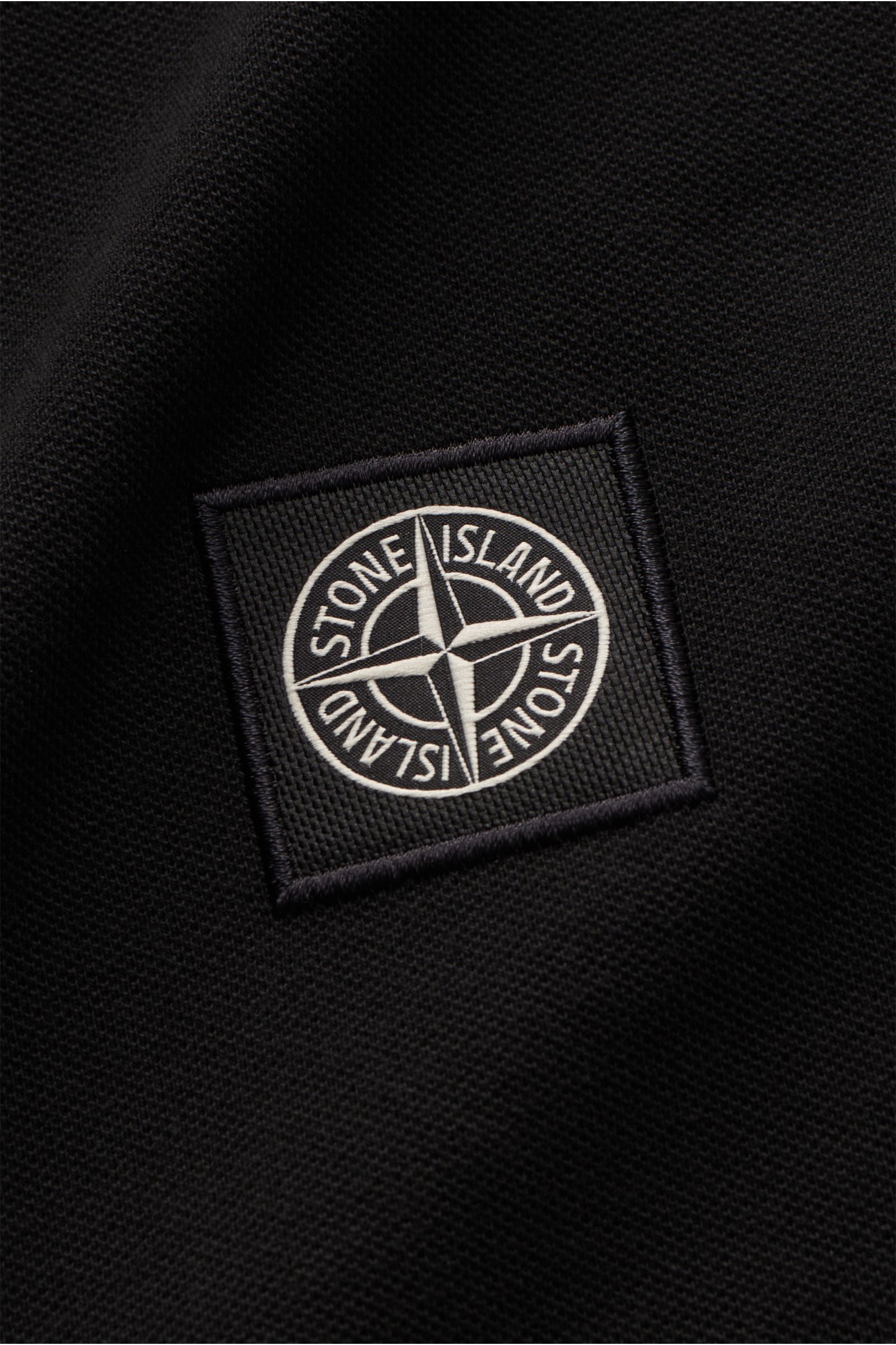 Stone Island Longsleeve-Poloshirt schwarz aus reiner Baumwolle mit griffiger Piqué-Struktur, tonalem Kompasslogo, Slim Fit, Polokragen mit Kontraststreifen, Knopfleiste und kurzen Seitenschlitzen, fotografiert in Nahaufnahme.