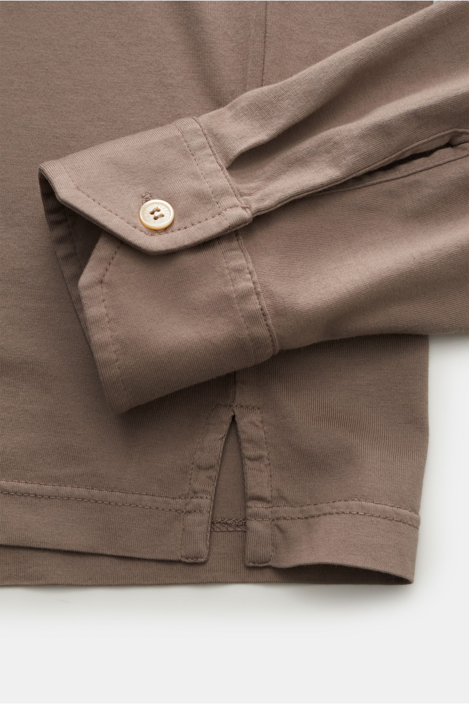 Close-up image of the Fedeli Jersey Longsleeve-Poloshirt 'Zero' taupe, showing the sleeve cuff with a mother-of-pearl button and the side hem slit, photographed from above. Sanfter und seidiger Griff: reine Giza-Baumwolle - zu komfortablem Jersey verar