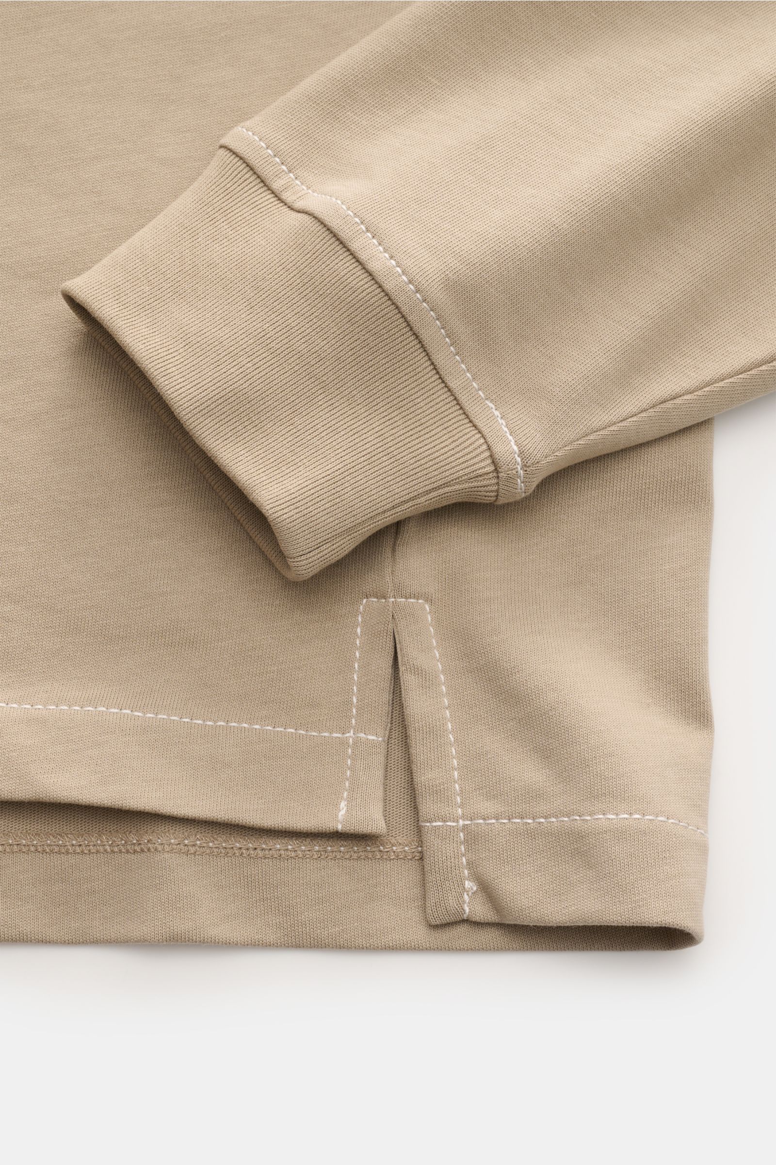 Close-up side view of Ami Paris Jersey long sleeve polo shirt taupe showing ribbed cuff, hem slit, and white contrast stitching on soft pure cotton fabric. Contemporary and casual: With its generous oversized fit, this long sleeve polo shirt by AMI PARIS 