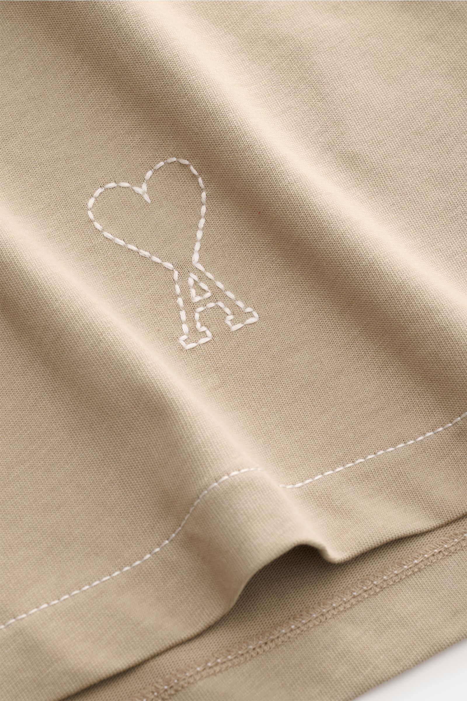 Close-up view of Ami Paris Jersey long sleeve polo shirt taupe fabric showing signature logo stitching, soft pure cotton jersey with oversized fit, dress-shirt collar, and three-button patch placket. Contemporary and casual: With its generous oversized fi