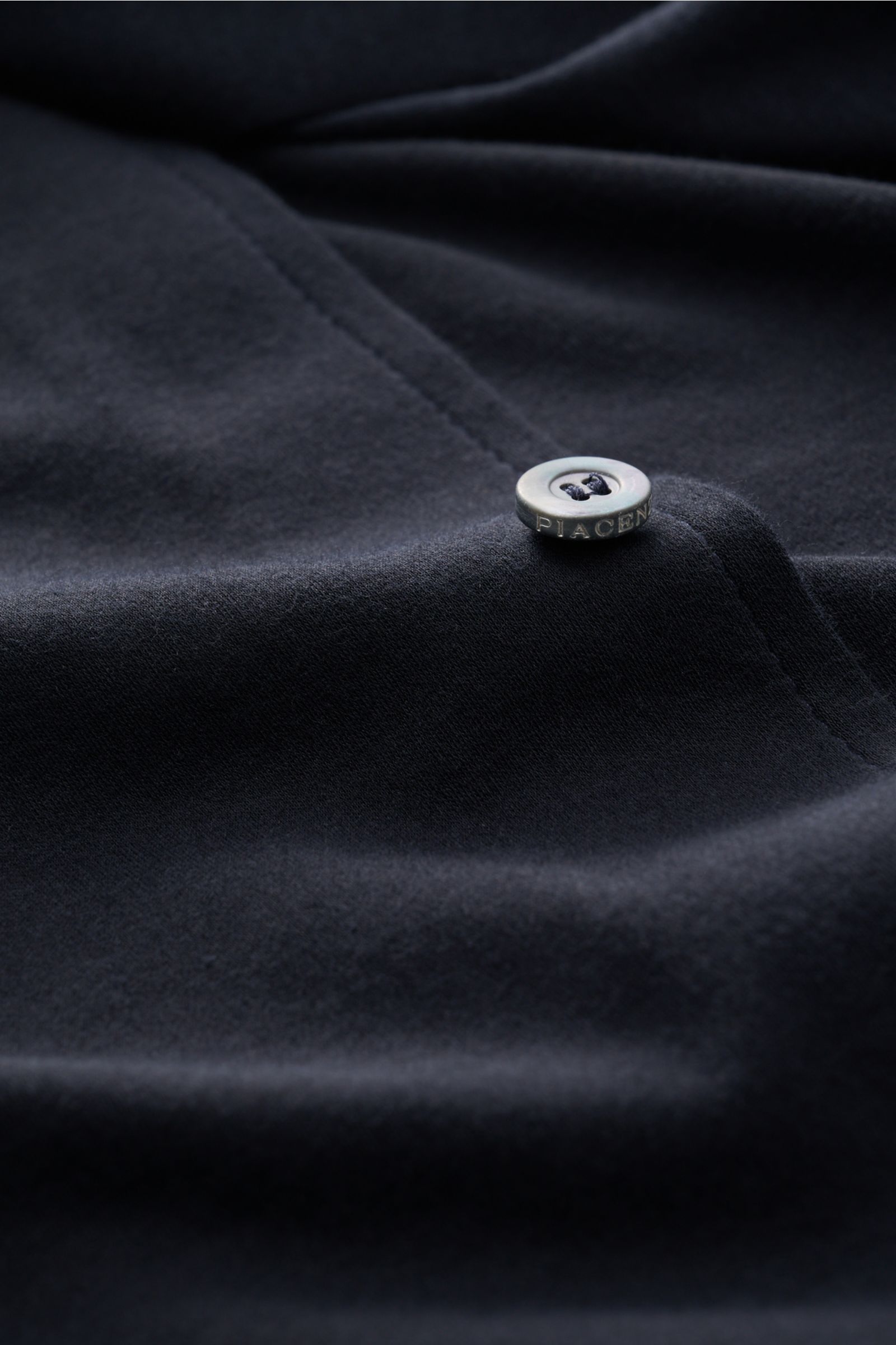 Nahaufnahme des Piacenza 1733 Jersey-Hemd schmaler Kragen dark navy mit weichem Baumwoll-Jersey, feinem Strickbild und eingeprägtem Knopf aus schräger Perspektive.