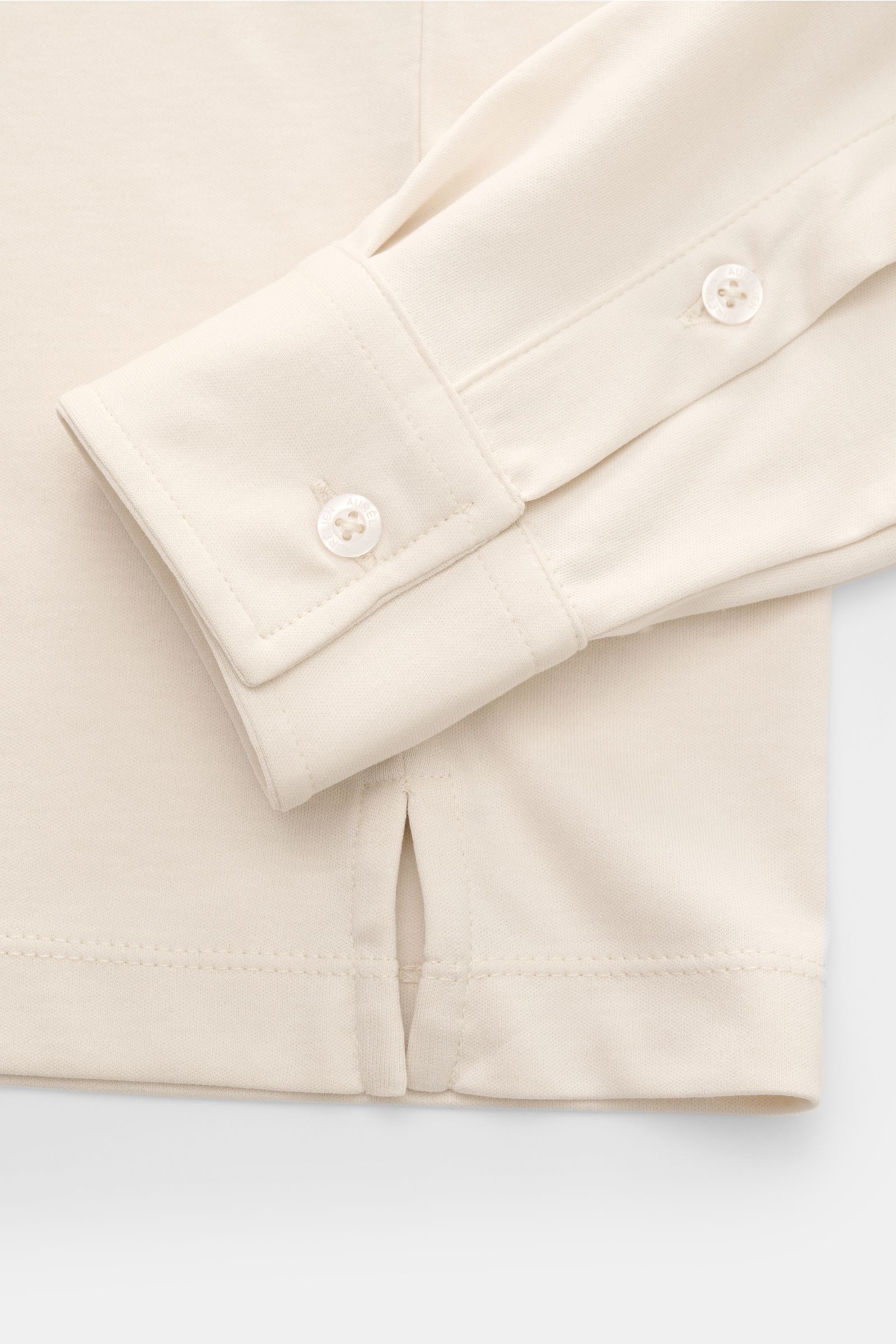 Close-up detail of the sleeve cuff and hem with side slit of the Aurélien Jersey Longsleeve-Poloshirt sand, photographed from above.

Description: Das vielseitig einsetzbare Longsleeve-Poloshirt der Marke AURÉLIEN wurde aus edler ägyptischer Baumwolle 