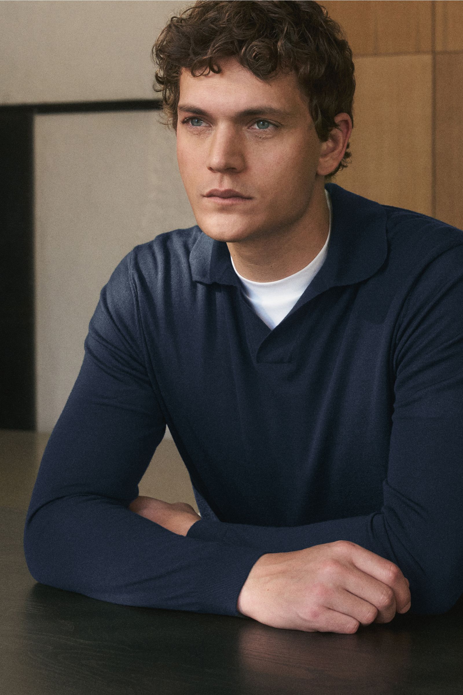 Mann von schräg vorne sitzend, trägt von Braun Merino Strickpolo navy aus reiner Merinowolle, offener Kragen, Regular Fit, elastische Rippbündchen.