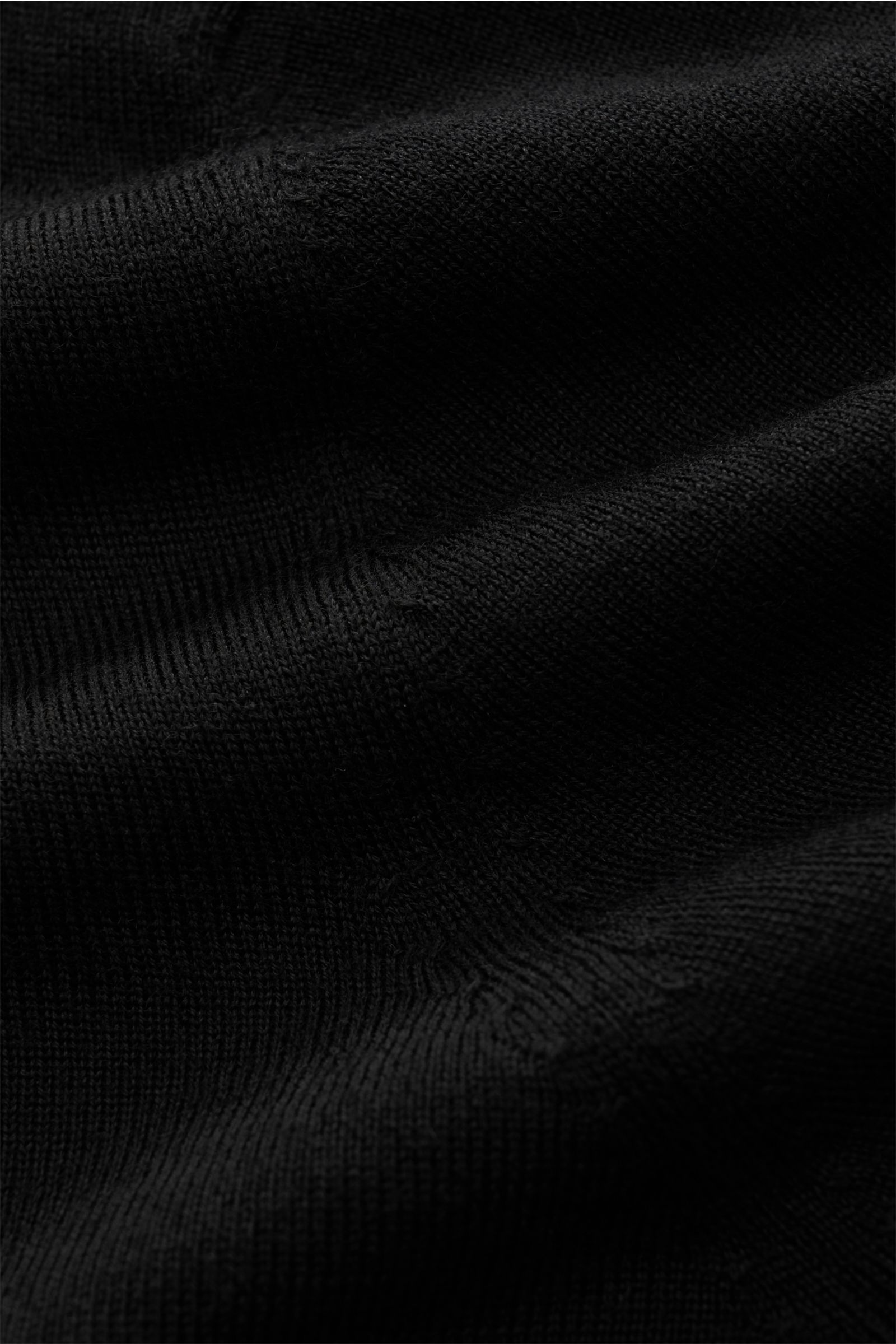 Nahaufnahme des schwarzen von Braun Merino Strickpolo, seitlich fotografiert, aus reiner Merinowolle mit offenem Kragen und feinem Strickbild.