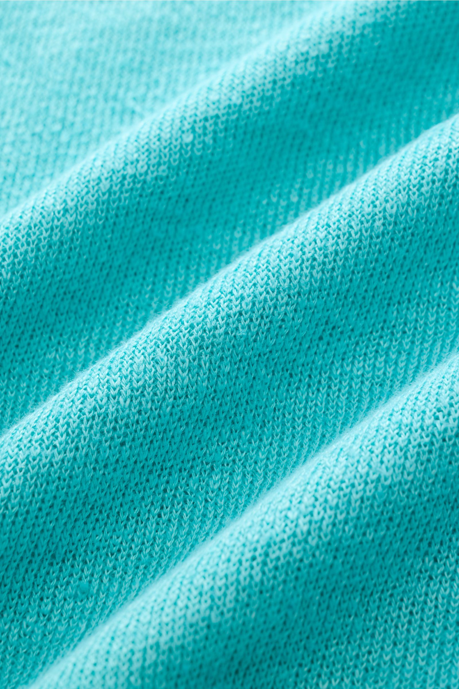 Nahaufnahme eines türkisfarbenen 04651/ A trip in a bag Polo, Stofftextur in diagonaler Perspektive.