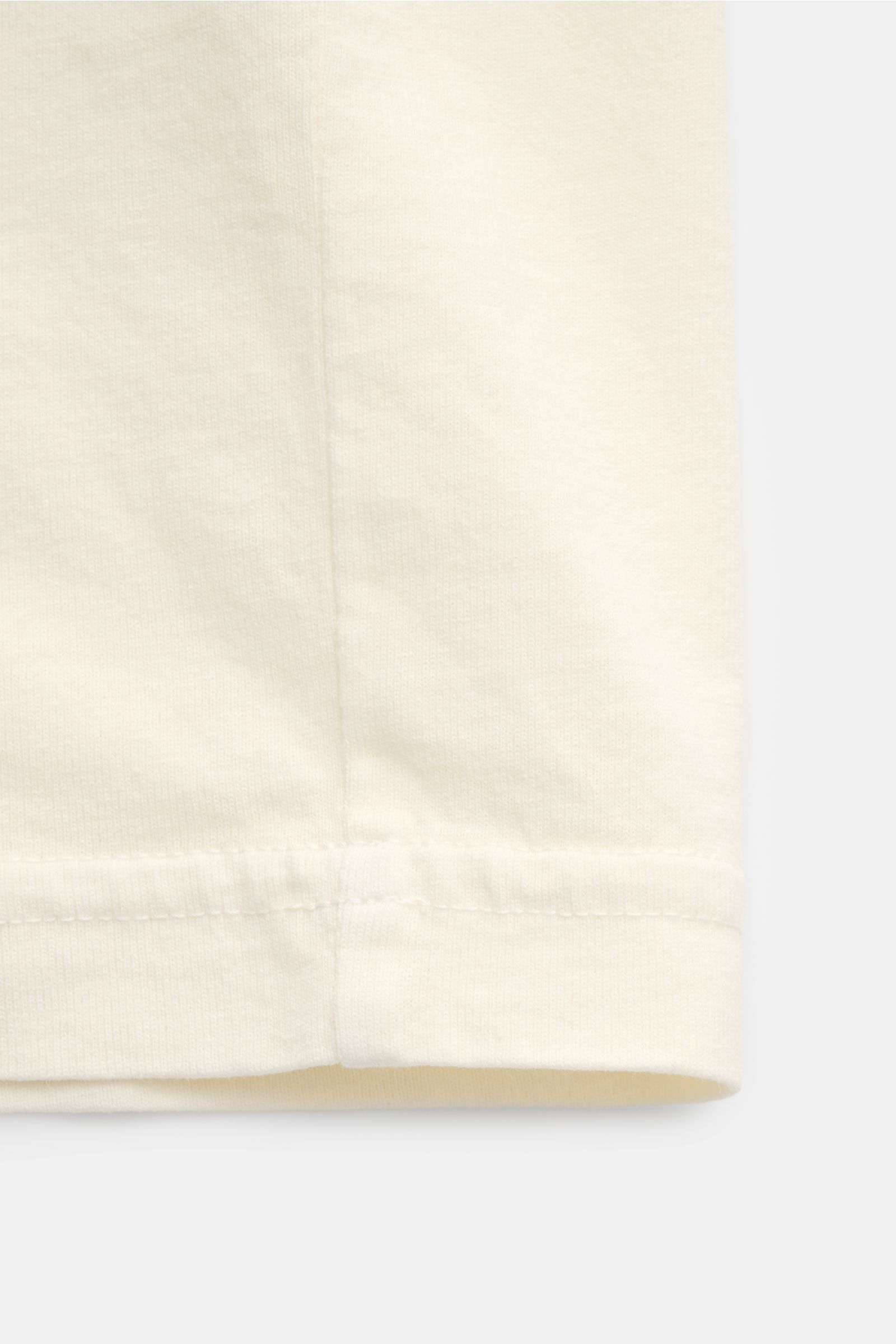 Nahaufnahme des Saums vom Stone Island Rundhals-T-Shirt 'Industrial Print' creme aus garment dyed Baumwolle mit leichter Haptik, fotografiert von vorne unten.
