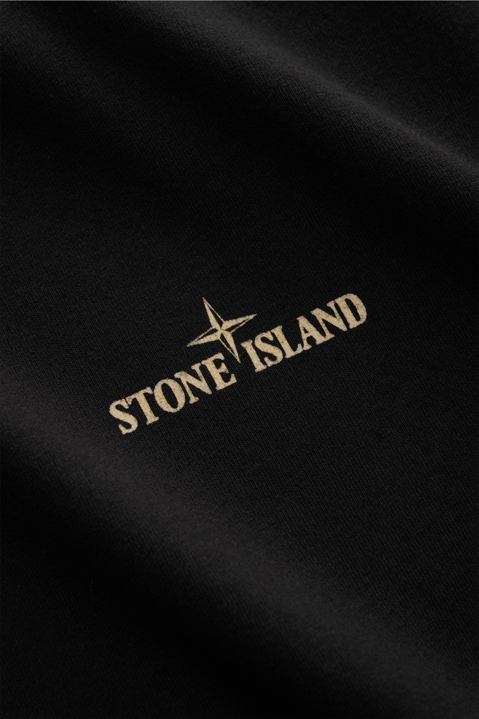 Close-up frontal view of the black Stone Island Rundhals-T-Shirt 'Industrial Print' schwarz showing the beige Stone Island logo and compass on garment-dyed cotton fabric.

STONE ISLAND liefert mit diesem legeren T-Shirt aus Garment-dyed-Baumwolle mit c