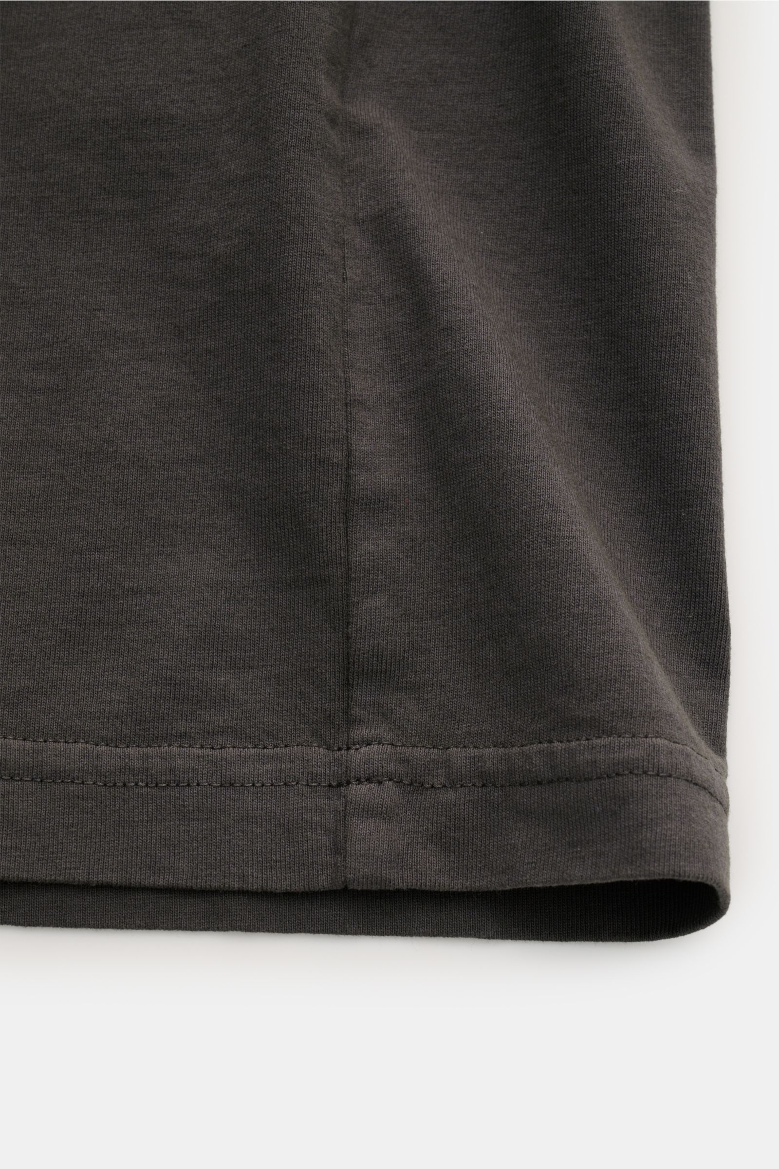Close-up of the hem and side seam of the Stone Island Rundhals-T-Shirt 'Industrial Print' dunkelgrau, showing dark gray garment-dyed cotton fabric with fine stitching from a side perspective.

STONE ISLAND liefert mit diesem legeren T-Shirt aus Garment