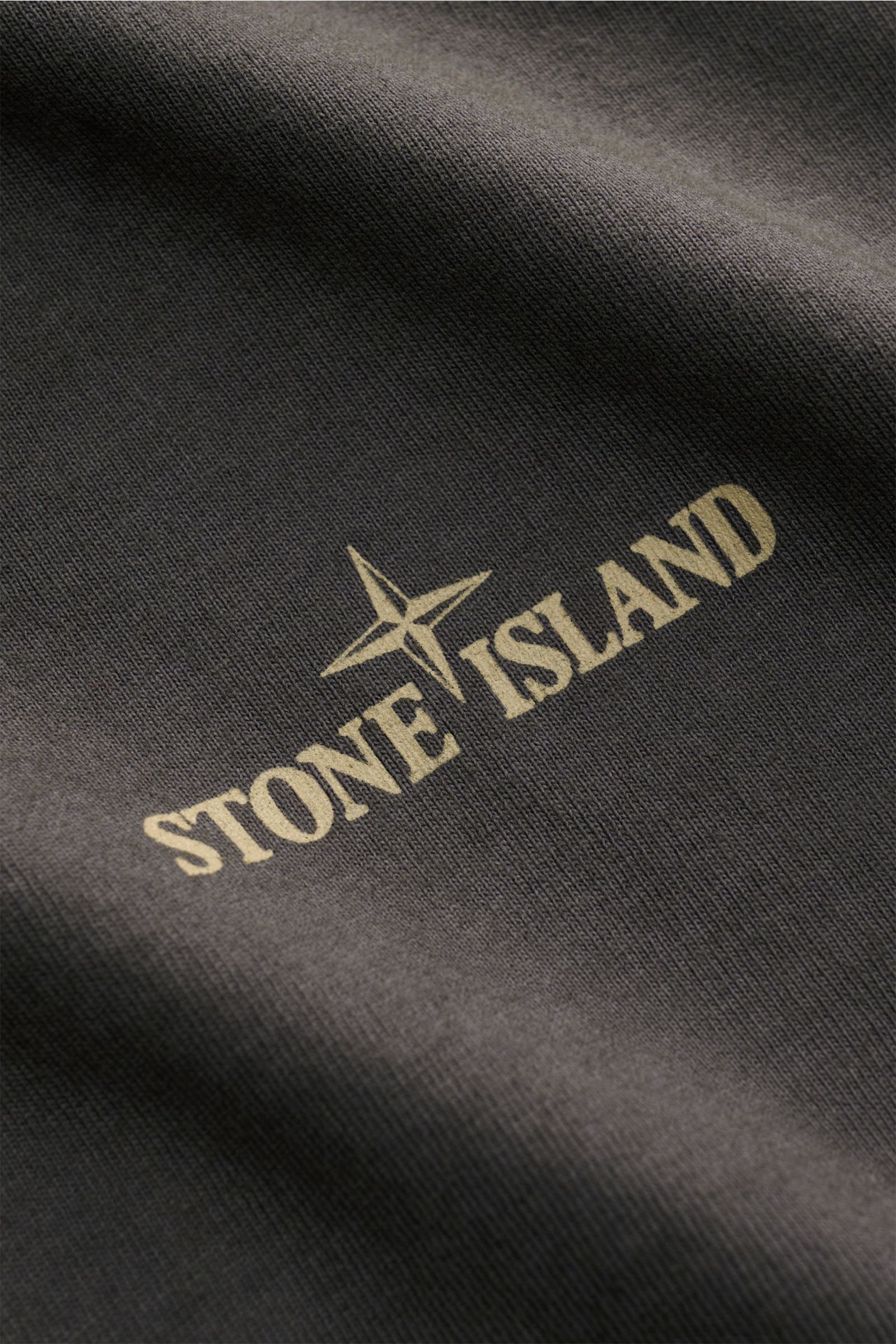 Close-up view of the Stone Island Rundhals-T-Shirt 'Industrial Print' dunkelgrau showing the beige STONE ISLAND logo and compass print on dark gray garment-dyed cotton fabric.

STONE ISLAND liefert mit diesem legeren T-Shirt aus Garment-dyed-Baumwolle 