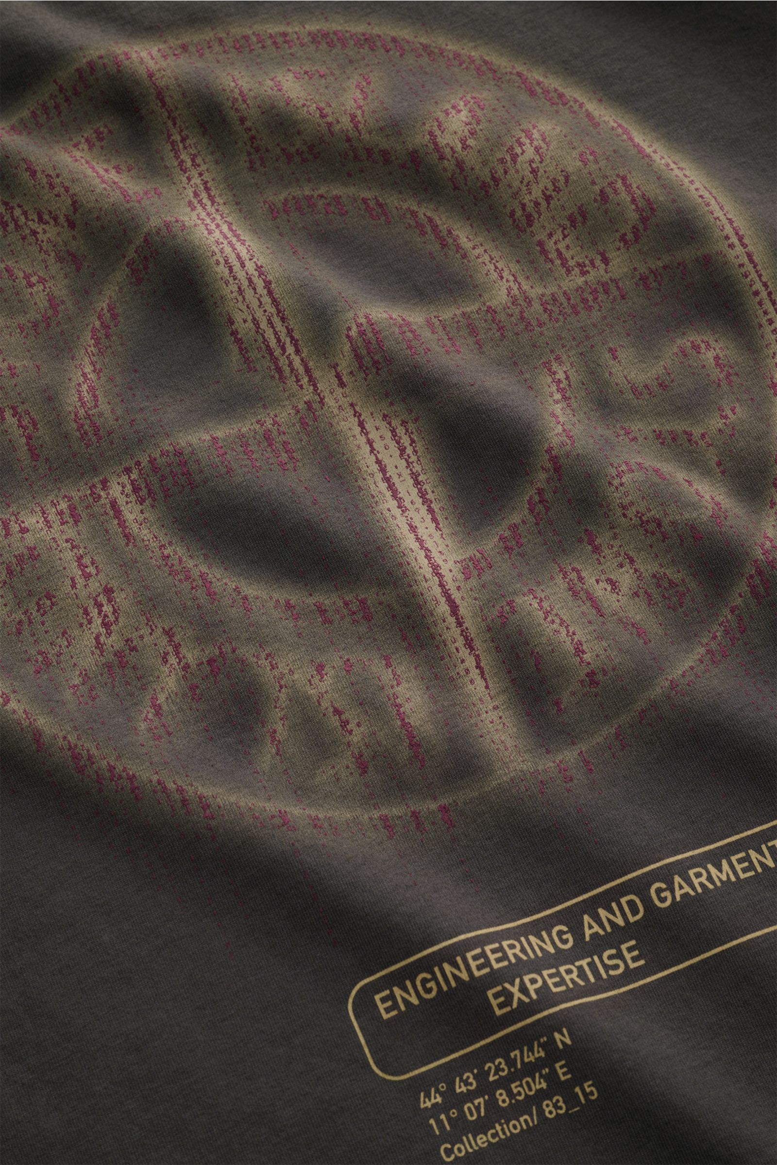 Close-up of the Stone Island Rundhals-T-Shirt 'Industrial Print' dunkelgrau showing the textured garment-dyed cotton fabric with a faded compass and Stone Island logo print from a top-down perspective.

Description: STONE ISLAND liefert mit diesem lege