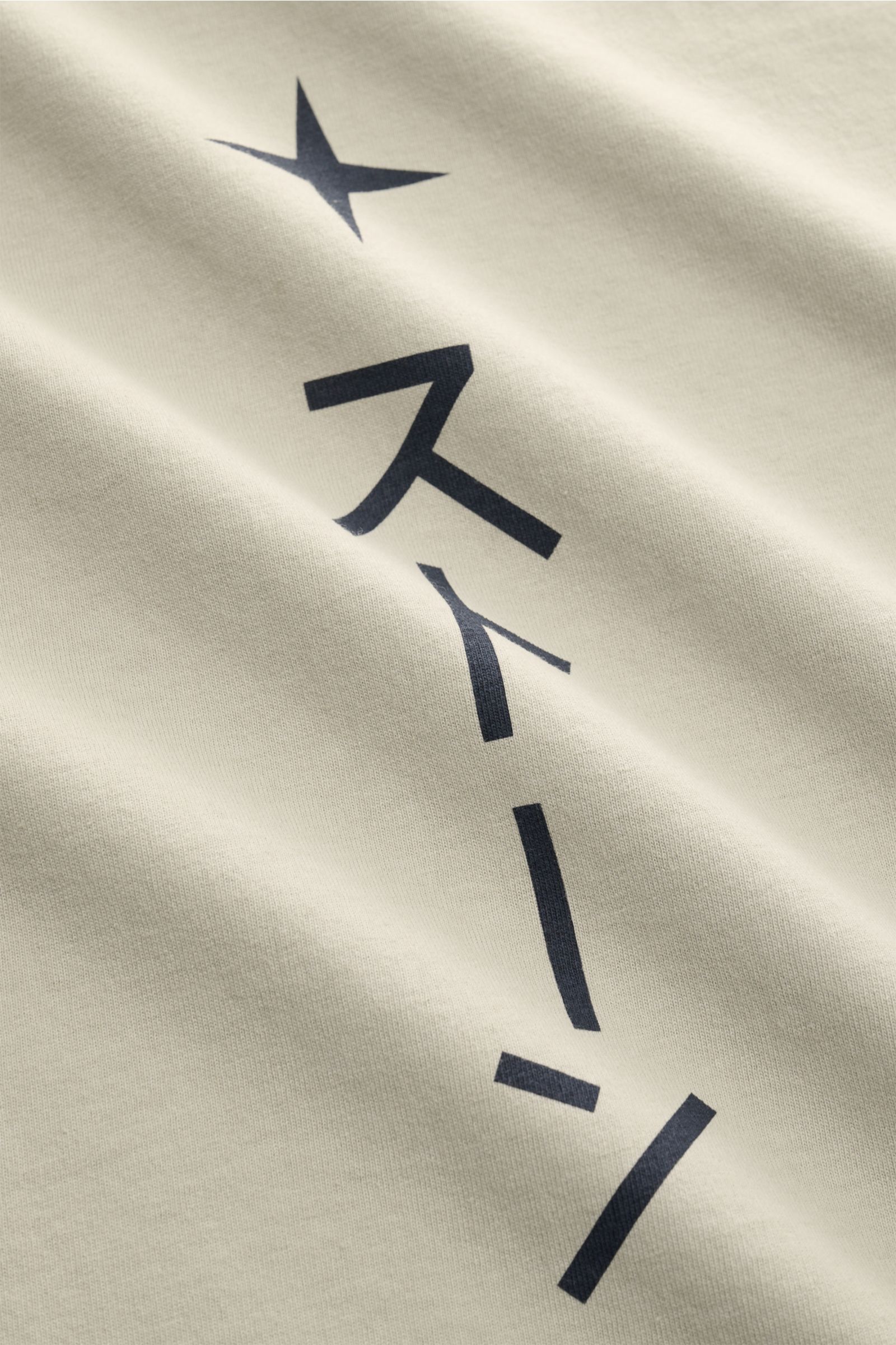 Close-up detail of the Stone Island Rundhals-T-Shirt sand showing a garment-dyed, heavy-quality, pure cotton jersey with a slightly textured feel, featuring a print on the front and a bold print on the back, photographed from an angled perspective to high