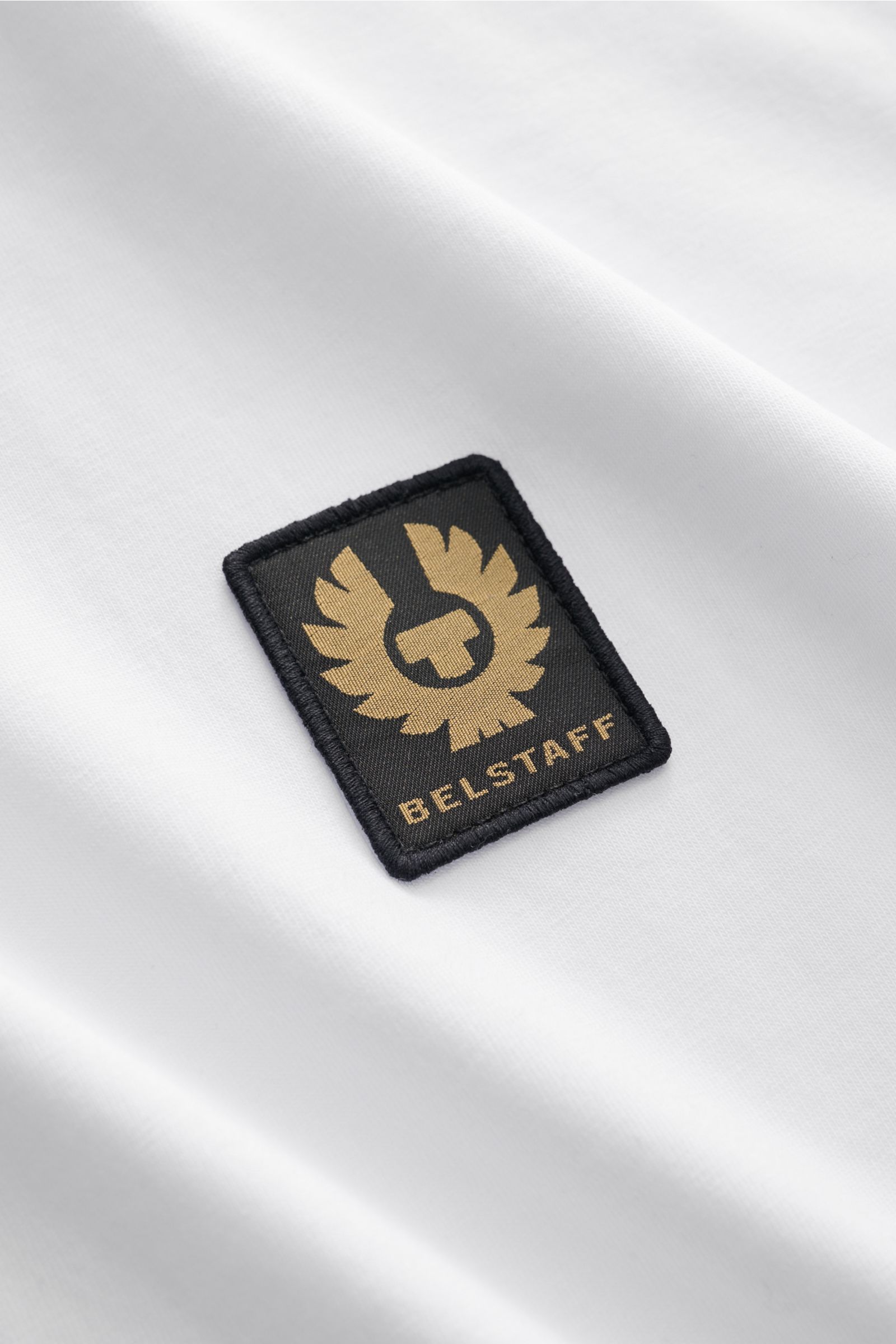 Close-up front view of the Belstaff Rundhals-T-Shirt weiß showing the black and gold BELSTAFF woven label on soft white cotton jersey fabric.

Dieses T-Shirt von BELSTAFF, gefertigt aus leichtem Baumwoll-Jersey und veredelt mit einem dezenten Weblabel,