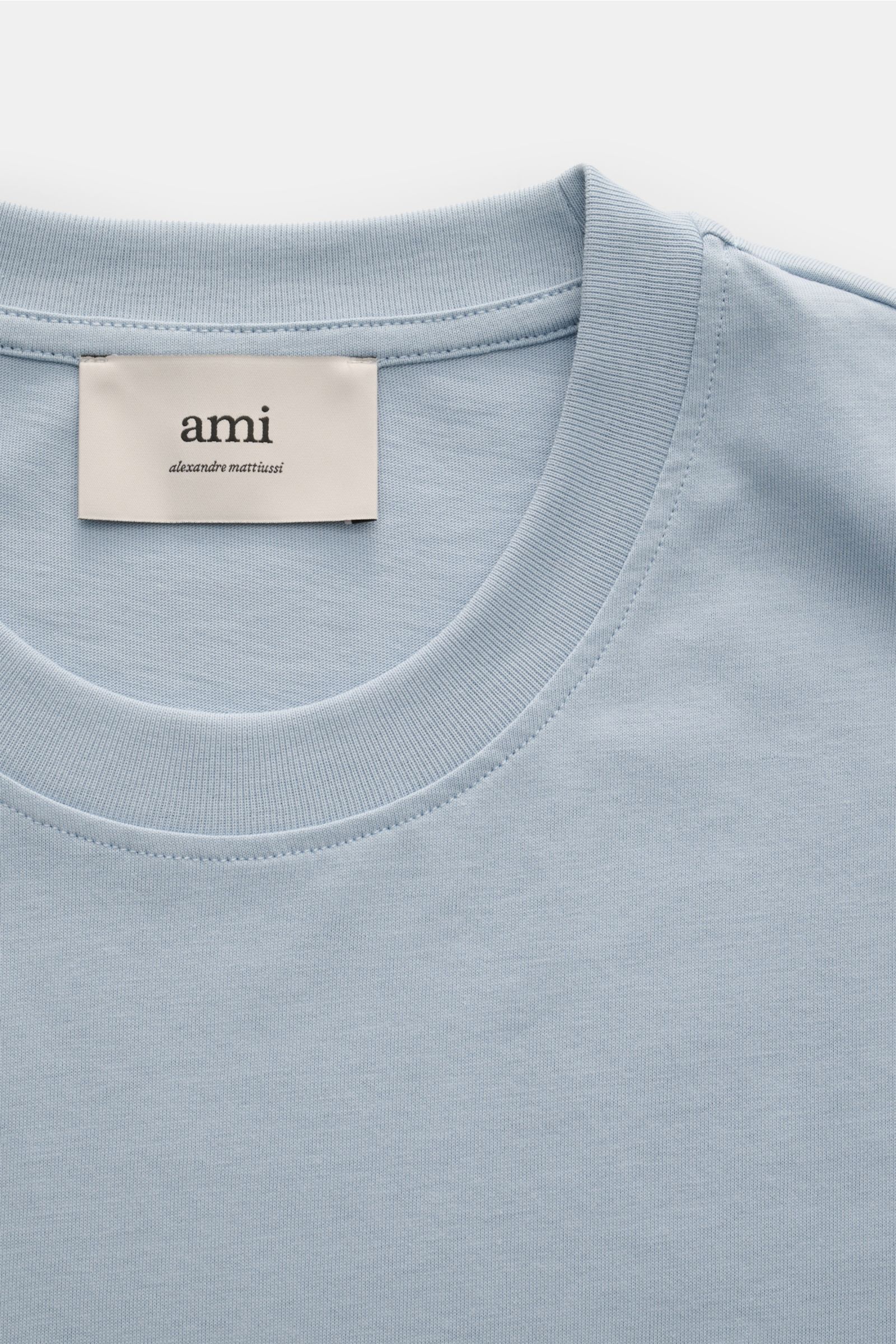 Close-up front view of Ami Paris Rundhals-T-Shirt rauchblau in soft, pure cotton jersey with round neckline and label inside collar.

Description: Klassisches Jersey-Basic vom französischen Label AMI PARIS: Dieses T-Shirt mit Rundhalsausschnitt ist aus