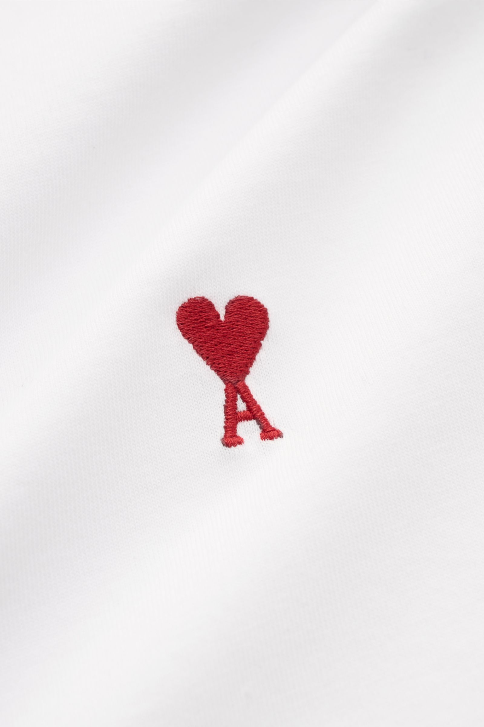 Close-up front view of the Ami Paris Rundhals-T-Shirt weiß showing soft white pure cotton jersey with red heart-stitching on the chest.  
Klassisches Jersey-Basic vom französischen Label AMI PARIS: Dieses T-Shirt mit Rundhalsausschnitt ist aus reiner B