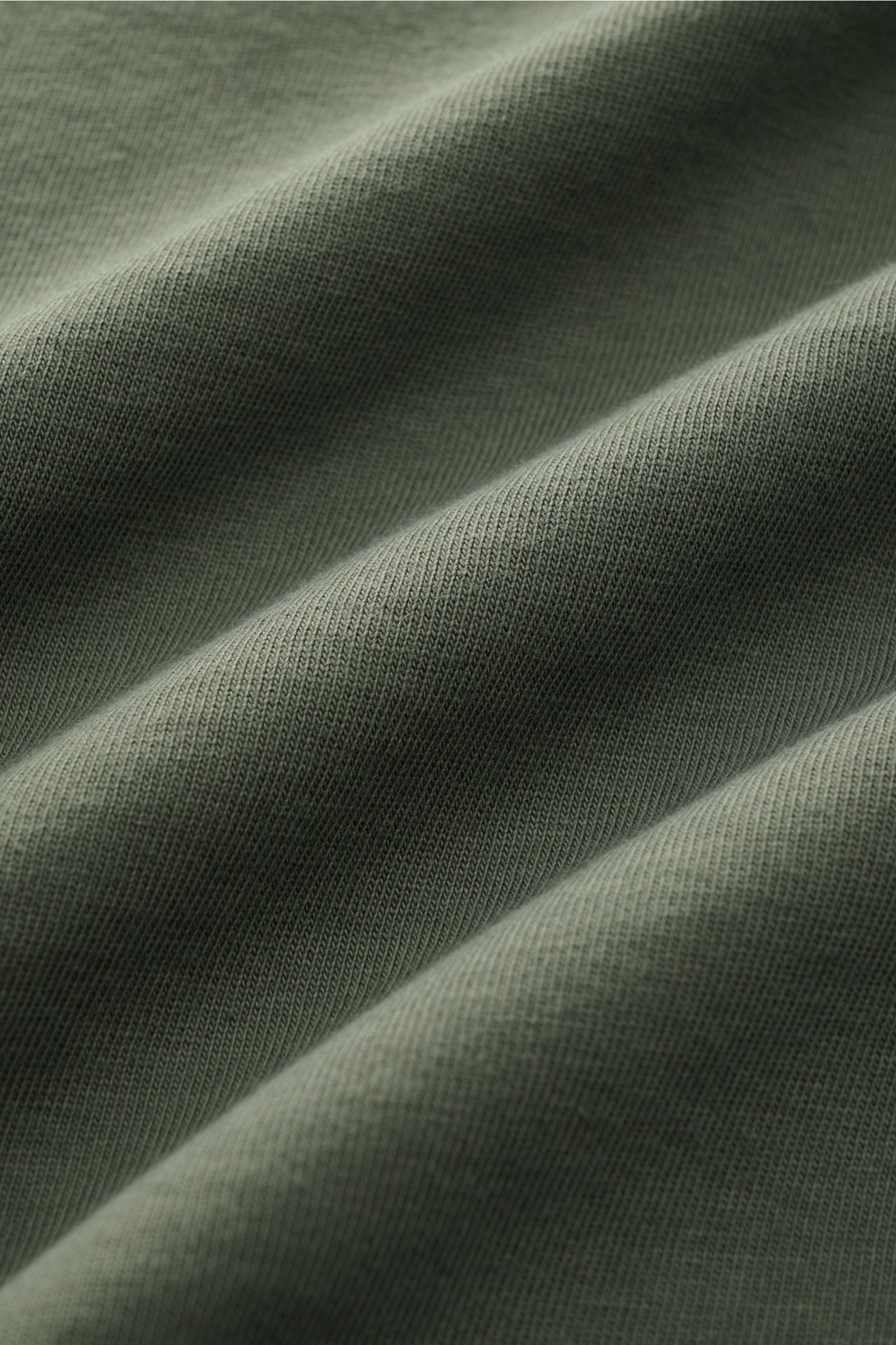 Close-up fabric detail of 04651/ A trip in a bag Rundhals-T-Shirt 'Nunu Tee' graugrün, photographed from above showing soft, grey-green cotton jersey texture. Tauchen Sie ein in den relaxten Lifestyle von 04651/ A TRIP IN A BAG – das unkomplizierte 'Nu