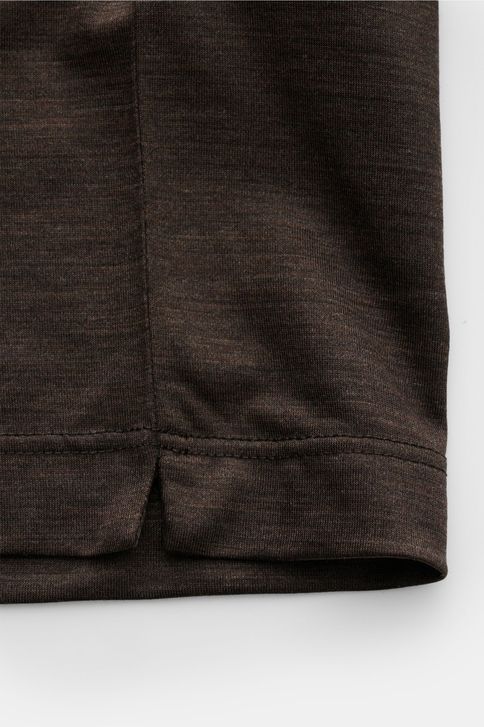 Close-up image of the hem with short side slits of the Marco Pescarolo Rundhals-T-Shirt 'James' dunkelbraun meliert, showing smooth, dark brown melange wool jersey fabric, photographed from a side angle. Für luxuriöse Woll-Verarbeitung steht MARCO PESCARO