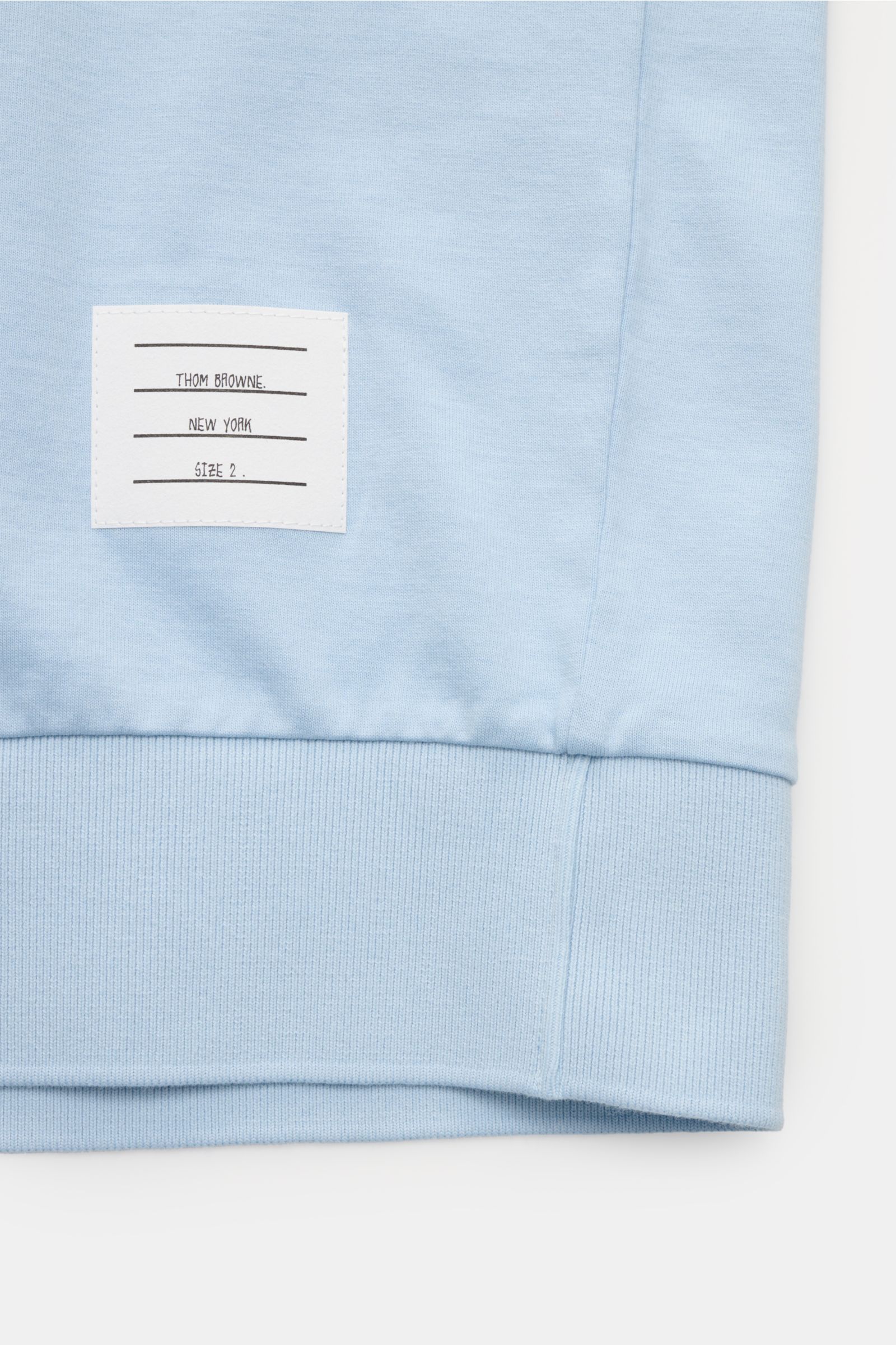 Close-up view of the wide hem and label on the Thom Browne Crew neck T-shirt smoky blue in heavy pure cotton jersey fabric.

Monochrome T-shirt by THOM BROWNE in heavy pure cotton jersey fabric refined with jumper-inspired bands – perfect for elegant s