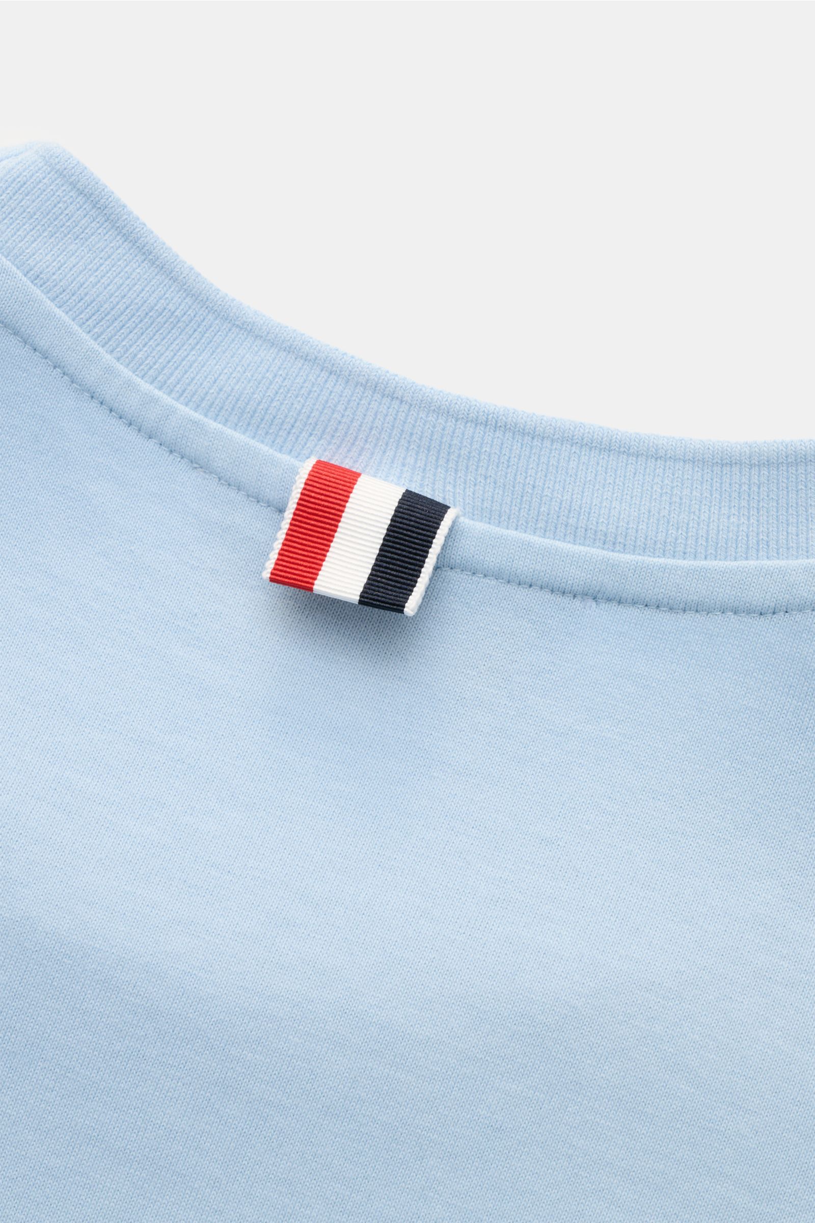Close-up view of the neck area of a Thom Browne Crew neck T-shirt smoky blue, showing fine stitching and the signature red, white, and navy jumper-inspired bands at the back.

Monochrome T-shirt by THOM BROWNE in heavy pure cotton jersey fabric refined