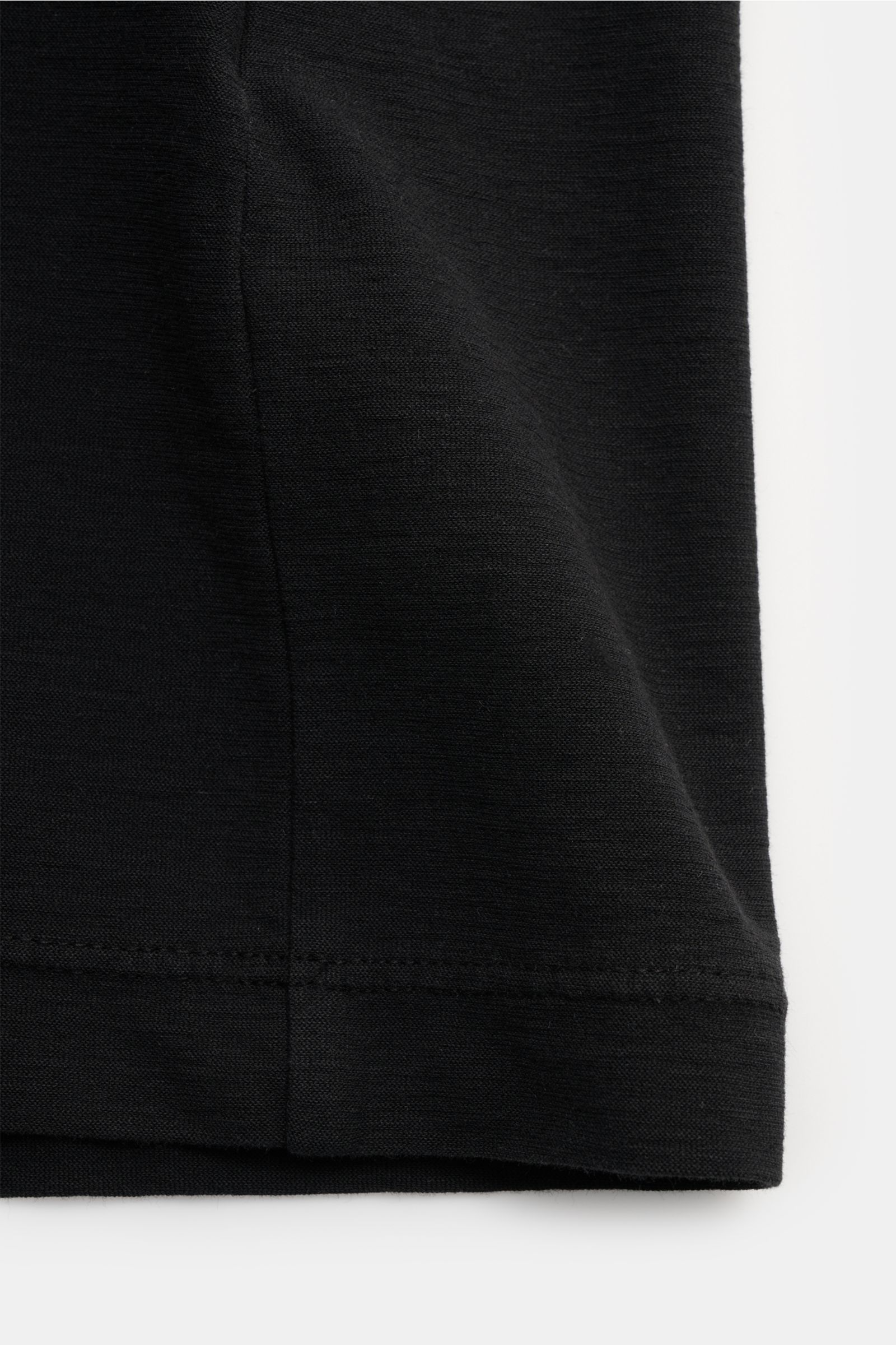 Close-up view of the hem and side seam of the Stone Island Rundhals-T-Shirt 'Ghost Piece' schwarz, made of elastic cotton jersey with a slightly textured feel, garment dyed, slim fit, featuring a tonal STONE ISLAND web label on the chest.
