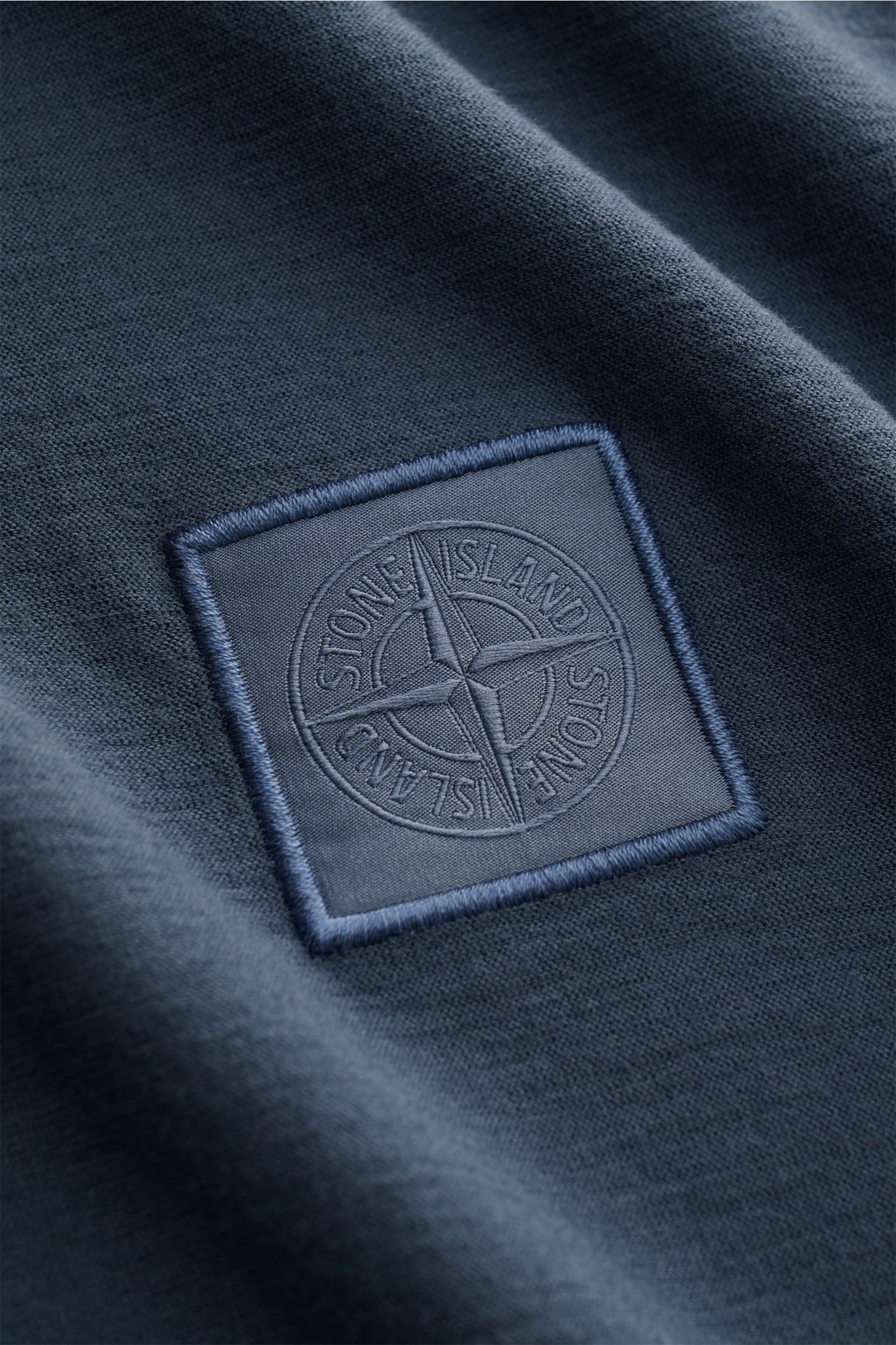 Close-up, angled view of the Stone Island Rundhals-T-Shirt 'Ghost Piece' graublau showing the tonal embroidered STONE ISLAND-Weblabel on soft, garment dyed cotton jersey fabric.

STONE ISLAND bietet mit dem Rundhals-T-Shirt aus elastischem Baumwolljers