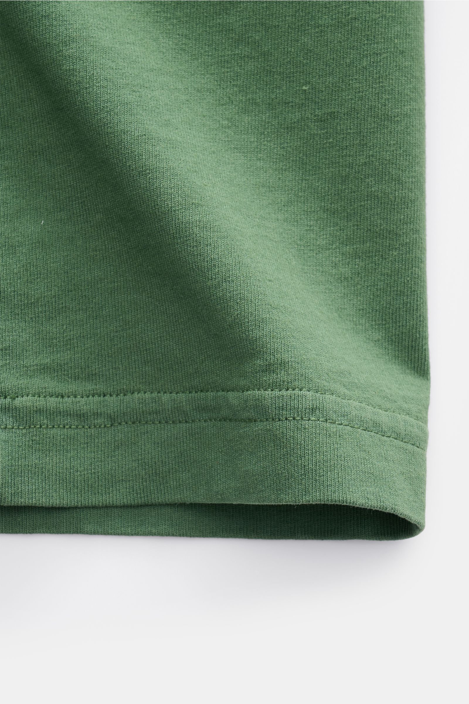 Close-up front view of the hem of the Stone Island Rundhals-T-Shirt 'Marina' grün in soft green cotton fabric, showing fine stitching and texture.

Legeres Urlaubs-Essential: Das T-Shirt aus der STONE ISLAND 'Marina' Capsule Collection steht für lässig