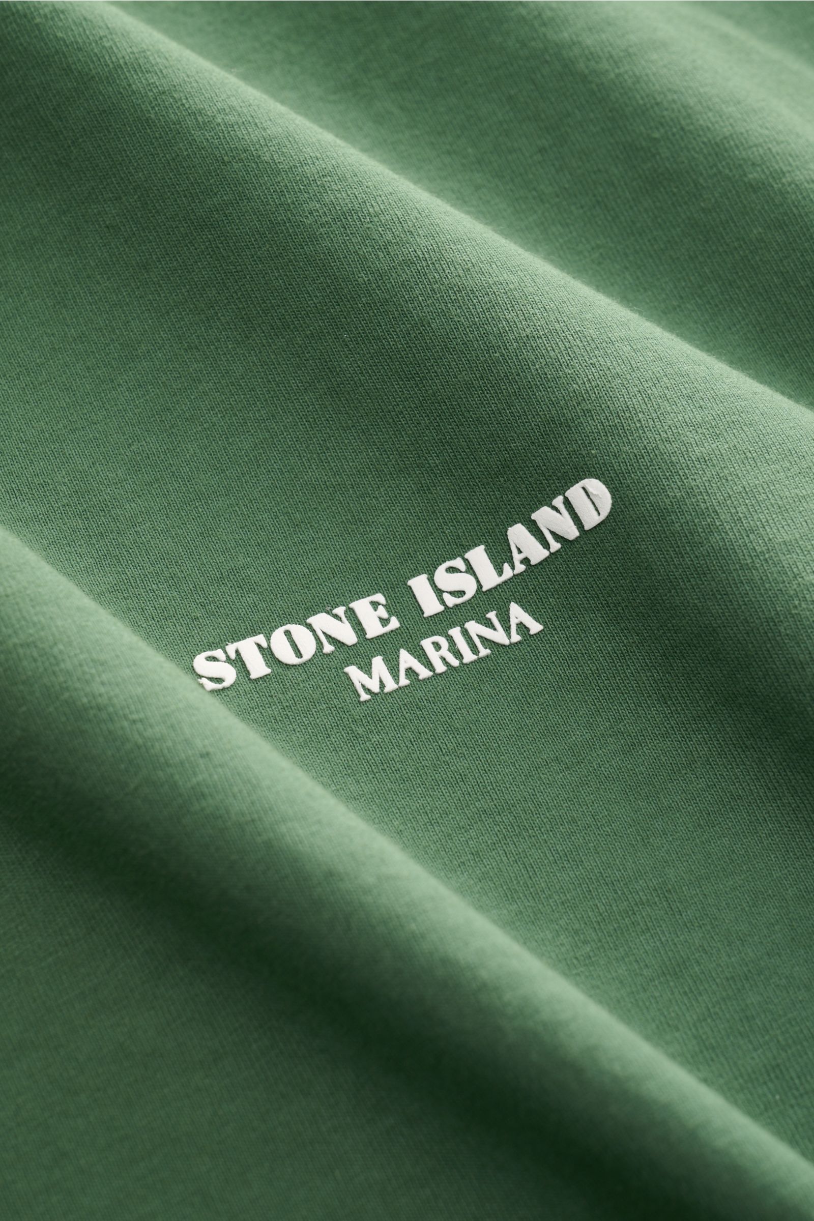 Close-up front view of the green Stone Island Rundhals-T-Shirt 'Marina' showing soft cotton fabric and white logo print.

Description: Legeres Urlaubs-Essential: Das T-Shirt aus der STONE ISLAND 'Marina' Capsule Collection steht für lässige Looks mit m