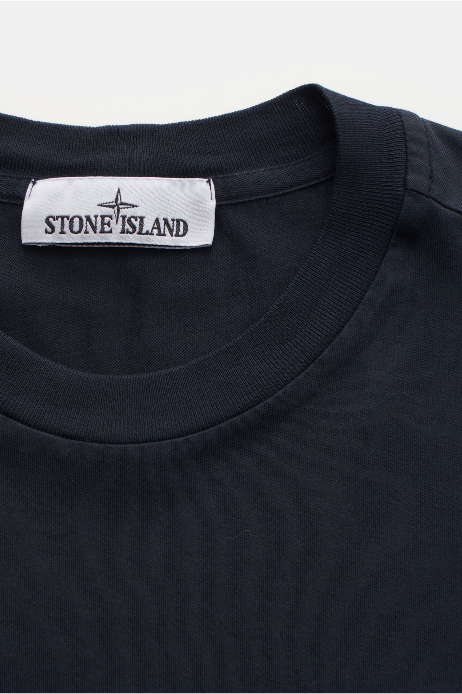 Nahaufnahme des Stone Island T-Shirts 'Basic Cotton' navy mit Rundhalsausschnitt, Weblabel auf der Brust, Slim Fit und weichem Griff aus reiner Baumwolle. Zeitloses Basic Piece für legere Freizeitlooks.