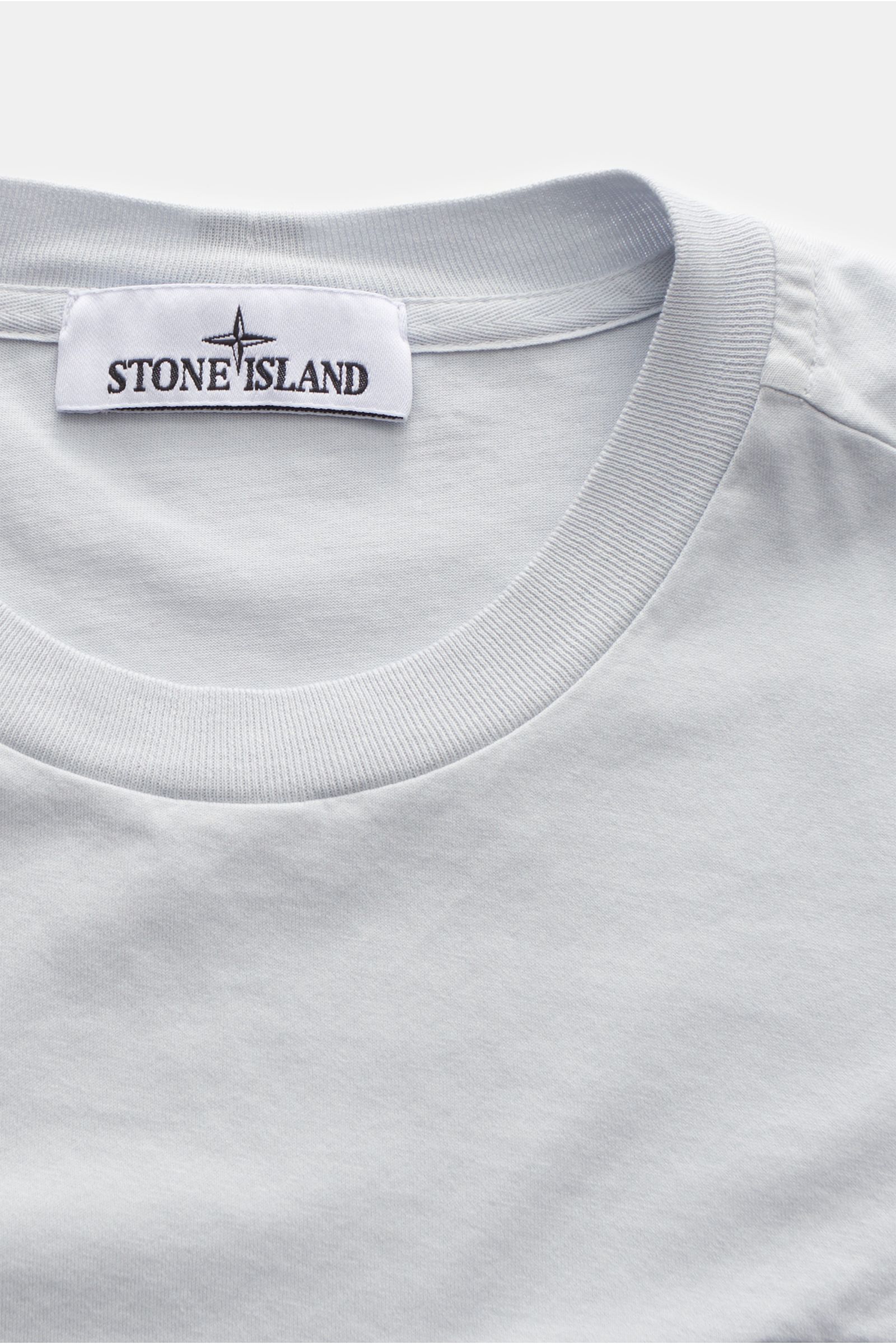 Stone Island T-Shirt 'Basic Cotton' pastellblau aus reiner Baumwolle, Slim Fit, weicher Griff, Rundhalsausschnitt, Weblabel auf Brust, Nahaufnahme von oben.