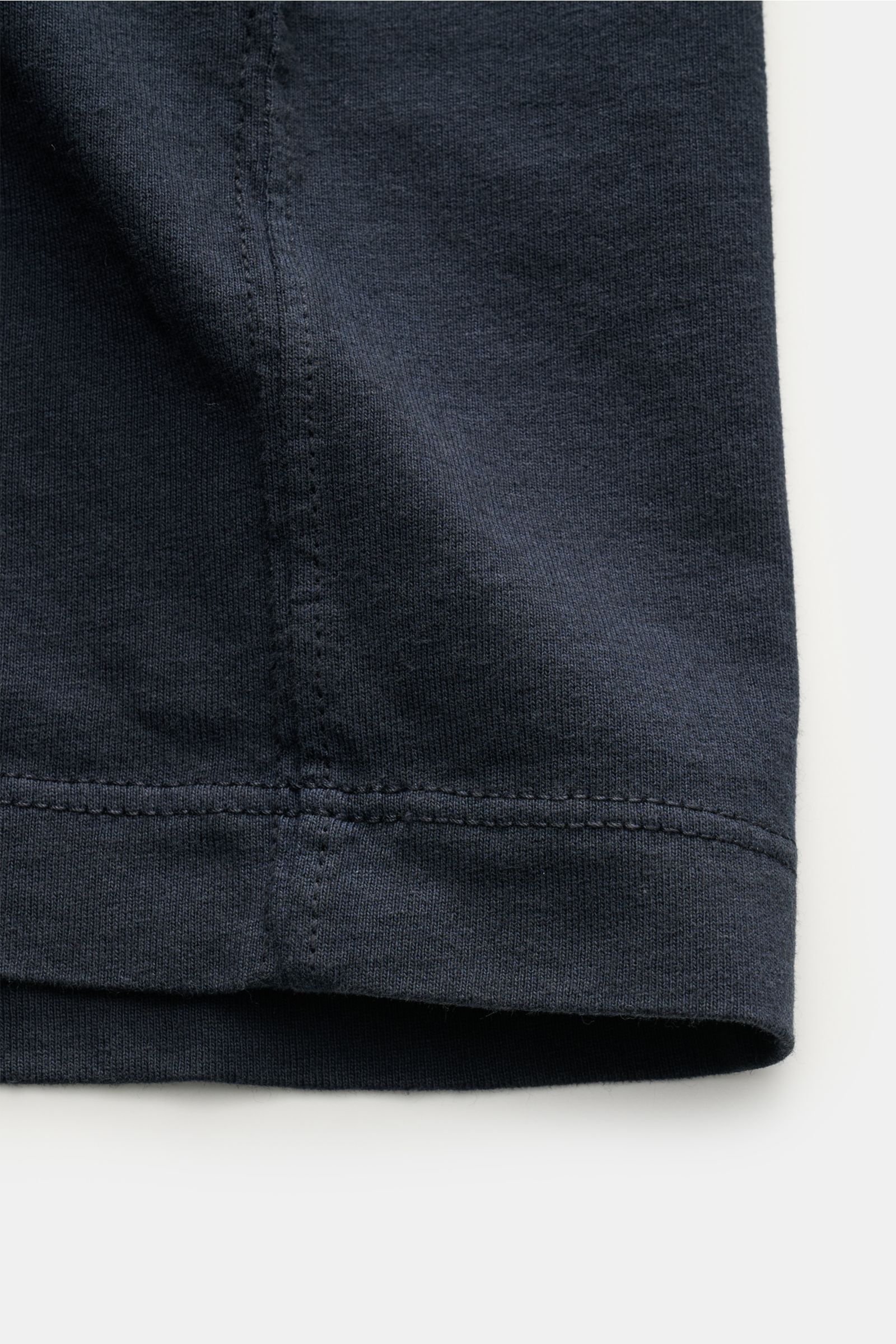 Nahaufnahme des unteren Saums vom Stone Island T-Shirt 'Dyed Regular Fit' navy aus reiner Baumwolle mit weichem Griff, Regular Fit, Rundhalsausschnitt und Weblabel auf der Brust, fotografiert von der Seite.