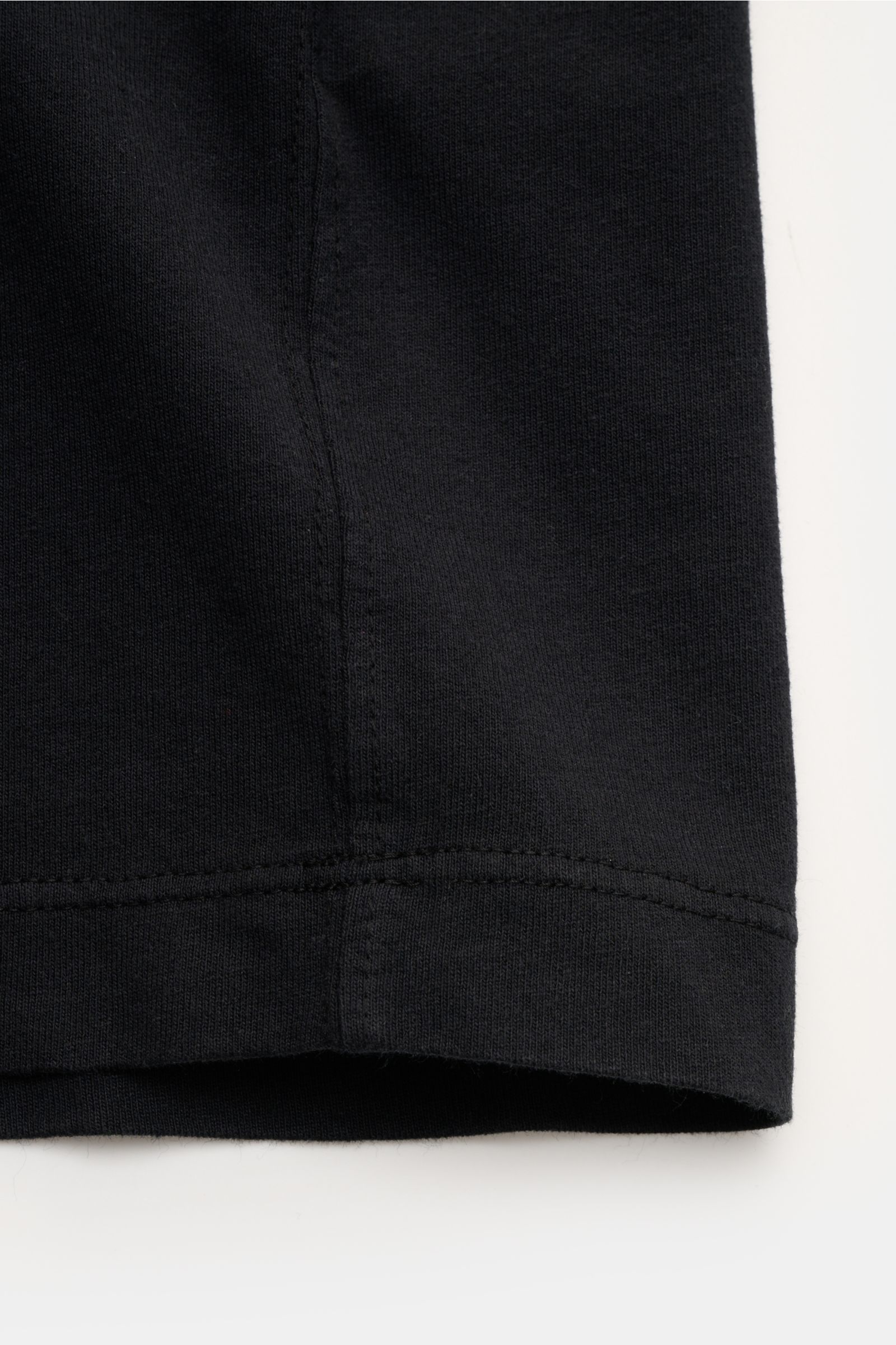 Nahaufnahme des unteren Saums eines schwarzen Stone Island T-Shirts 'Dyed Regular Fit', reine Bio-Baumwolle, weicher Griff, Regular Fit, Rundhalsausschnitt, Weblabel auf der Brust, fotografiert von vorne unten.