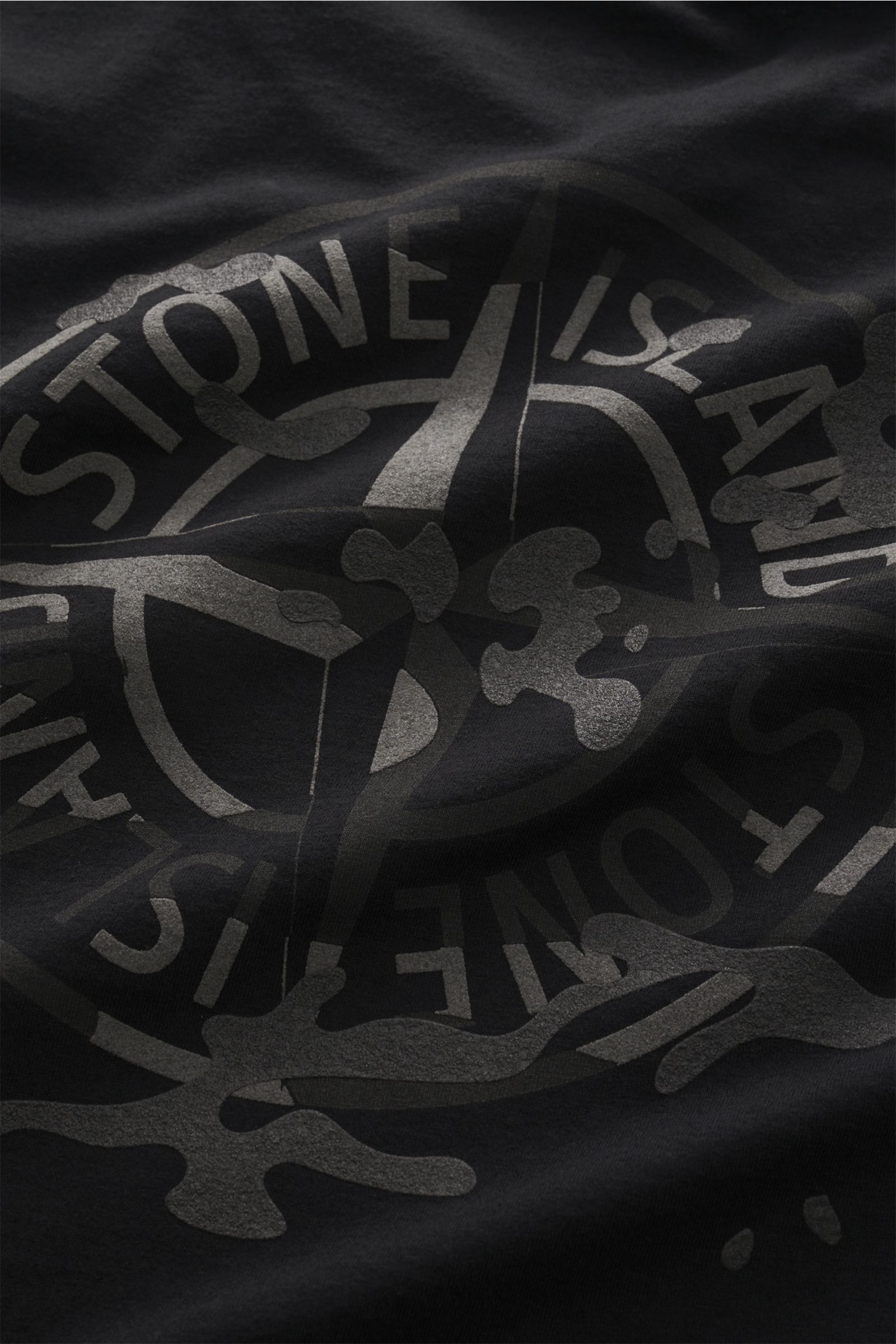 Nahaufnahme des Stone Island Rundhals-T-Shirts schwarz mit weichem Griff, schwerer Baumwolle und plakativem Rückenprint, von oben fotografiert.