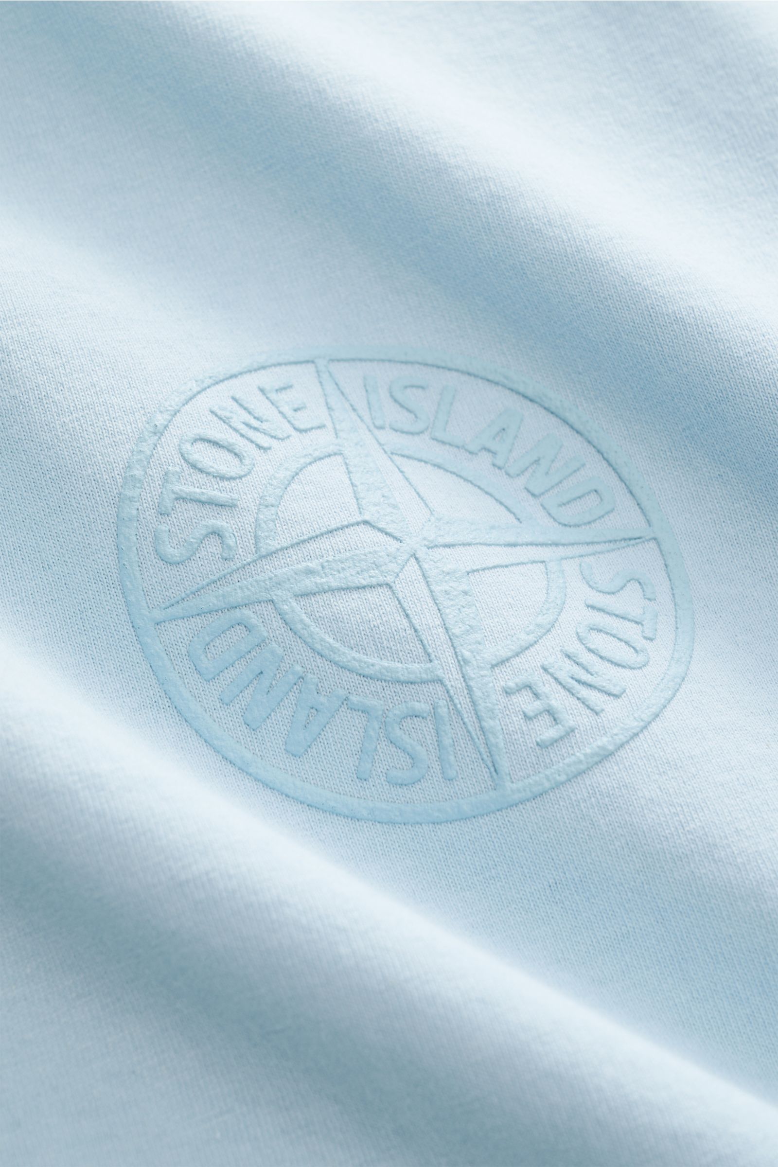Nahaufnahme des Stone Island Rundhals-T-Shirts hellblau mit prägnantem, tonalem Frontprint aus reiner Baumwolle, weicher Griff.