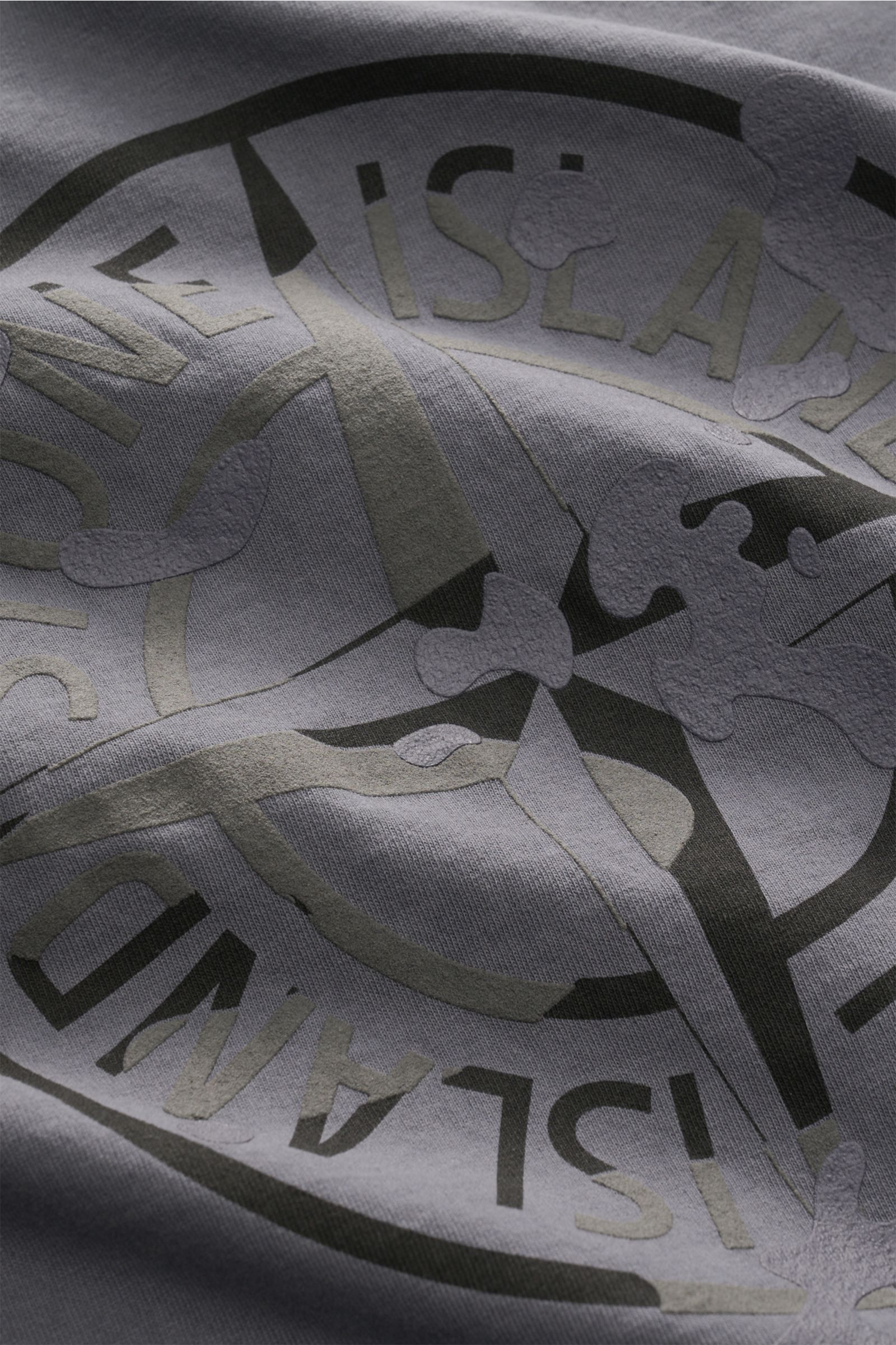 Nahaufnahme des plakativen Rückenprints auf dem Stone Island Rundhals-T-Shirt dunkelgrau, aufgenommen aus schräger Perspektive. Markantes Casual-Basic aus schwerer Baumwollqualität mit weichem Griff, Regular Fit, Rundhalsausschnitt und STONE ISLAND-Print 