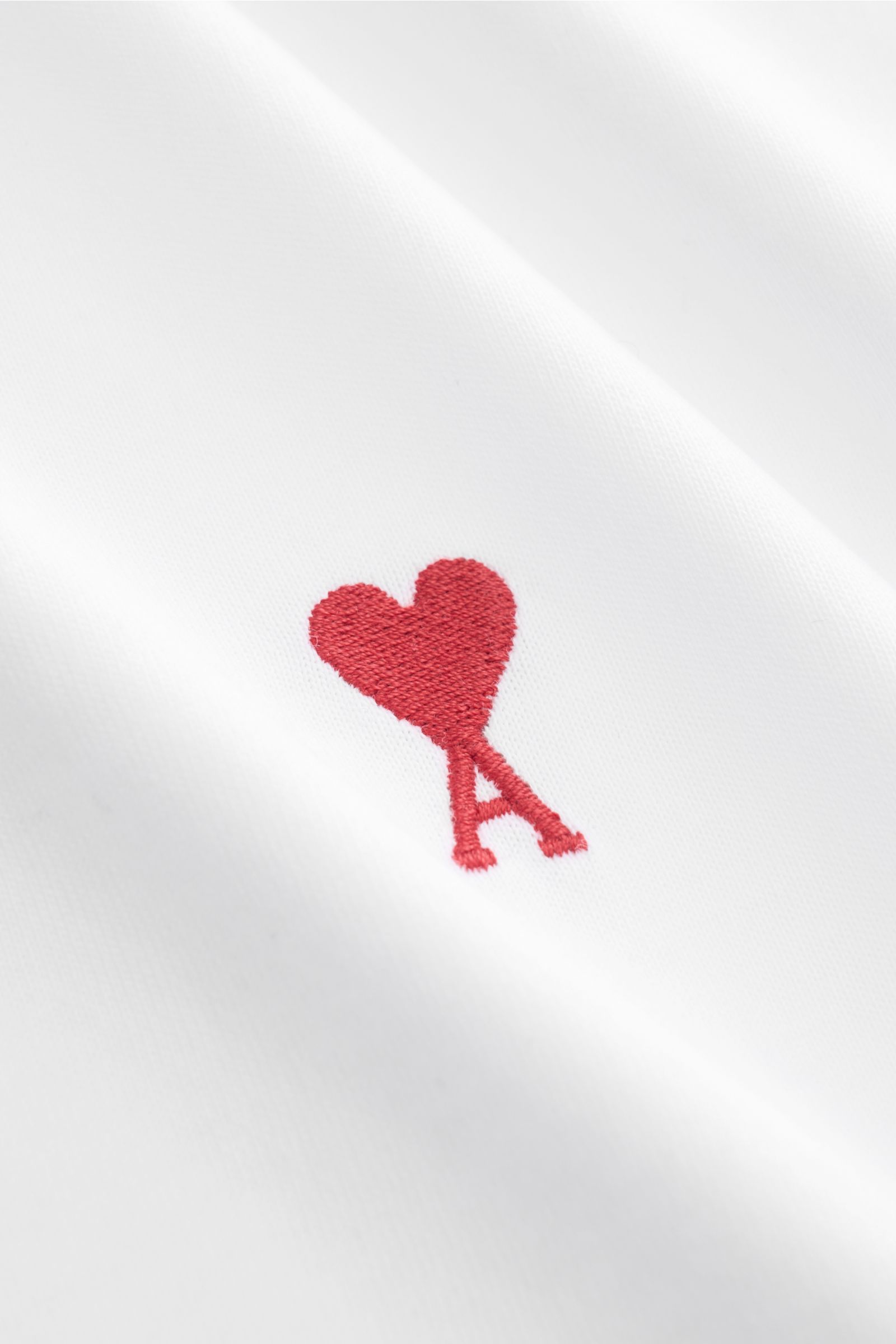 Detailaufnahme des roten Herz-Stitchings auf der Brust des weißen Ami Paris Rundhals-T-Shirts aus reiner Baumwolle.