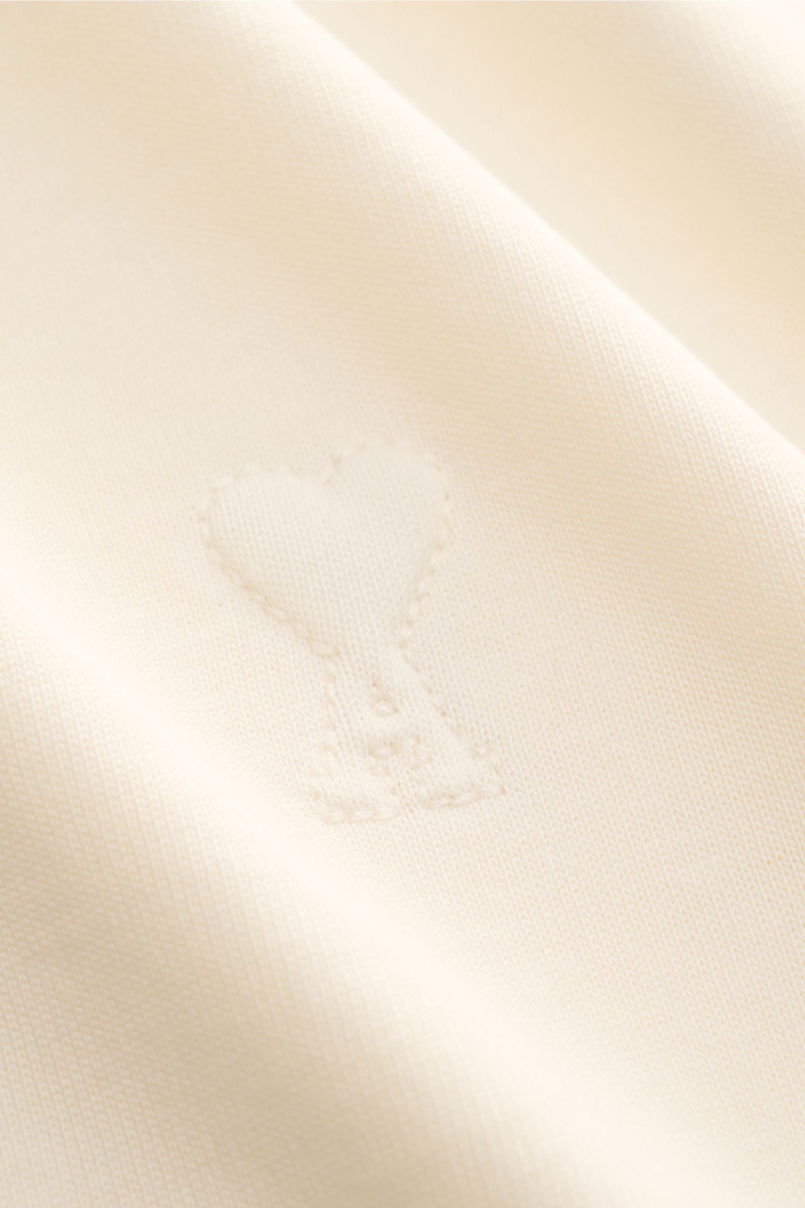 Ami Paris Rundhals-T-Shirt creme in Oversized Fit, Detailaufnahme des abgesteppte Herz-Logos aus weichem Baumwoll-Jersey.