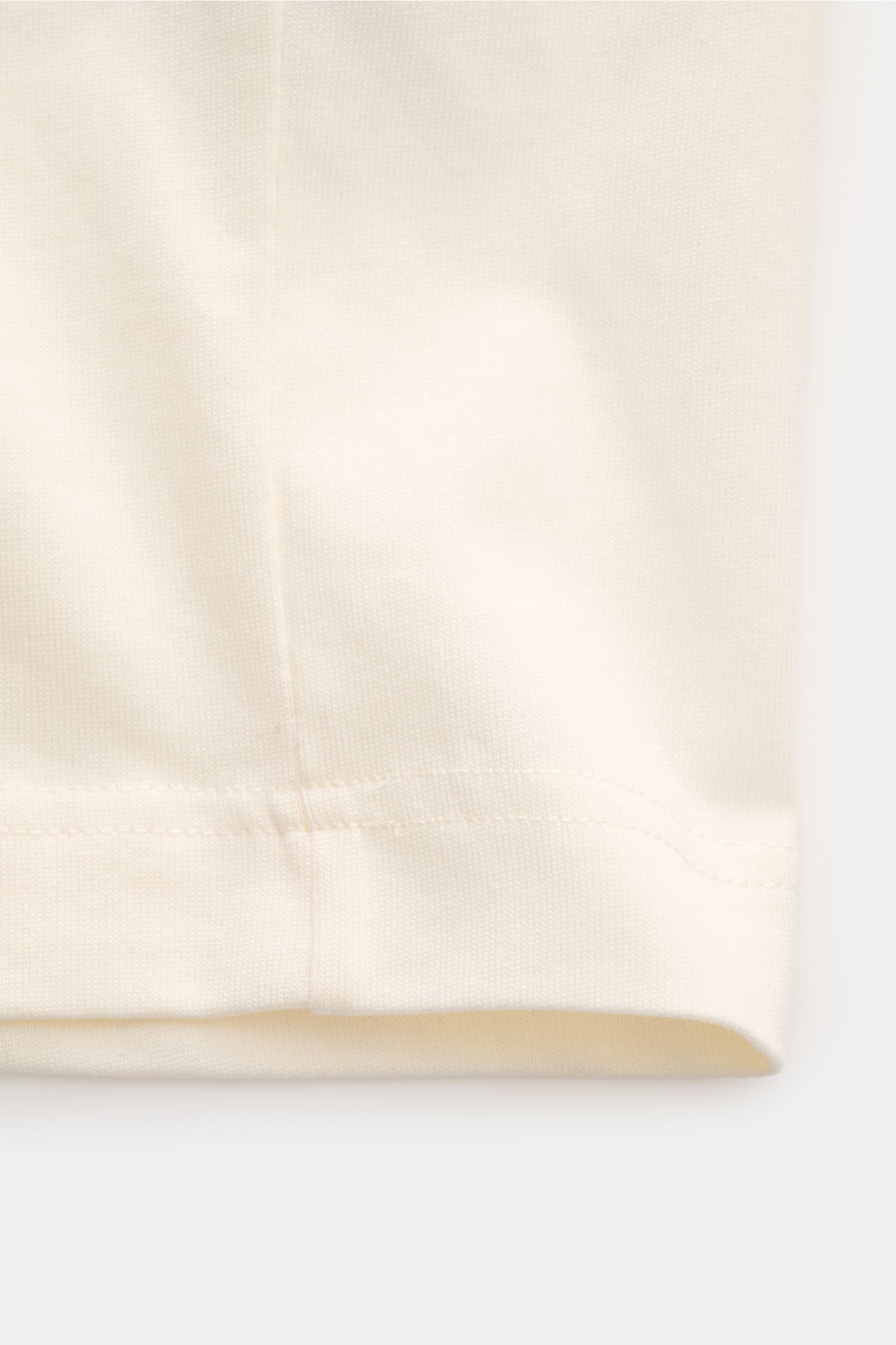 Close-up image of the hem and fabric texture of the Ami Paris Rundhals-T-Shirt creme, photographed from a side angle. Monochromes Jersey-Basic vom französischen Label AMI PARIS: Dieses T-Shirt mit Rundhalsausschnitt ist aus reiner Bio-Baumwolle gearbei