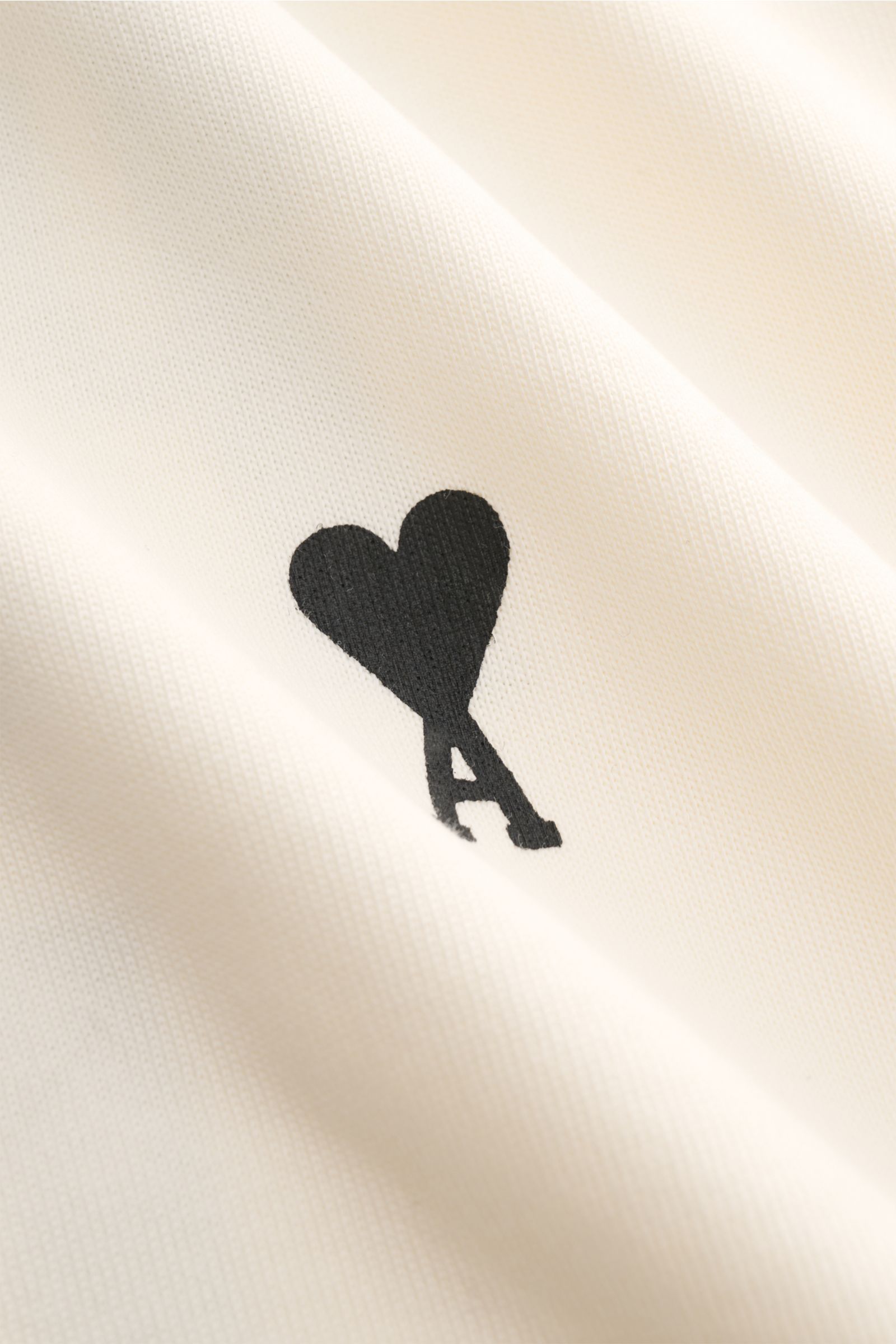 Close-up front view of Ami Paris Rundhals-T-Shirt creme showing the tonal stitched black heart logo on soft organic cotton jersey fabric. 

Monochromes Jersey-Basic vom französischen Label AMI PARIS: Dieses T-Shirt mit Rundhalsausschnitt ist aus reiner Bi