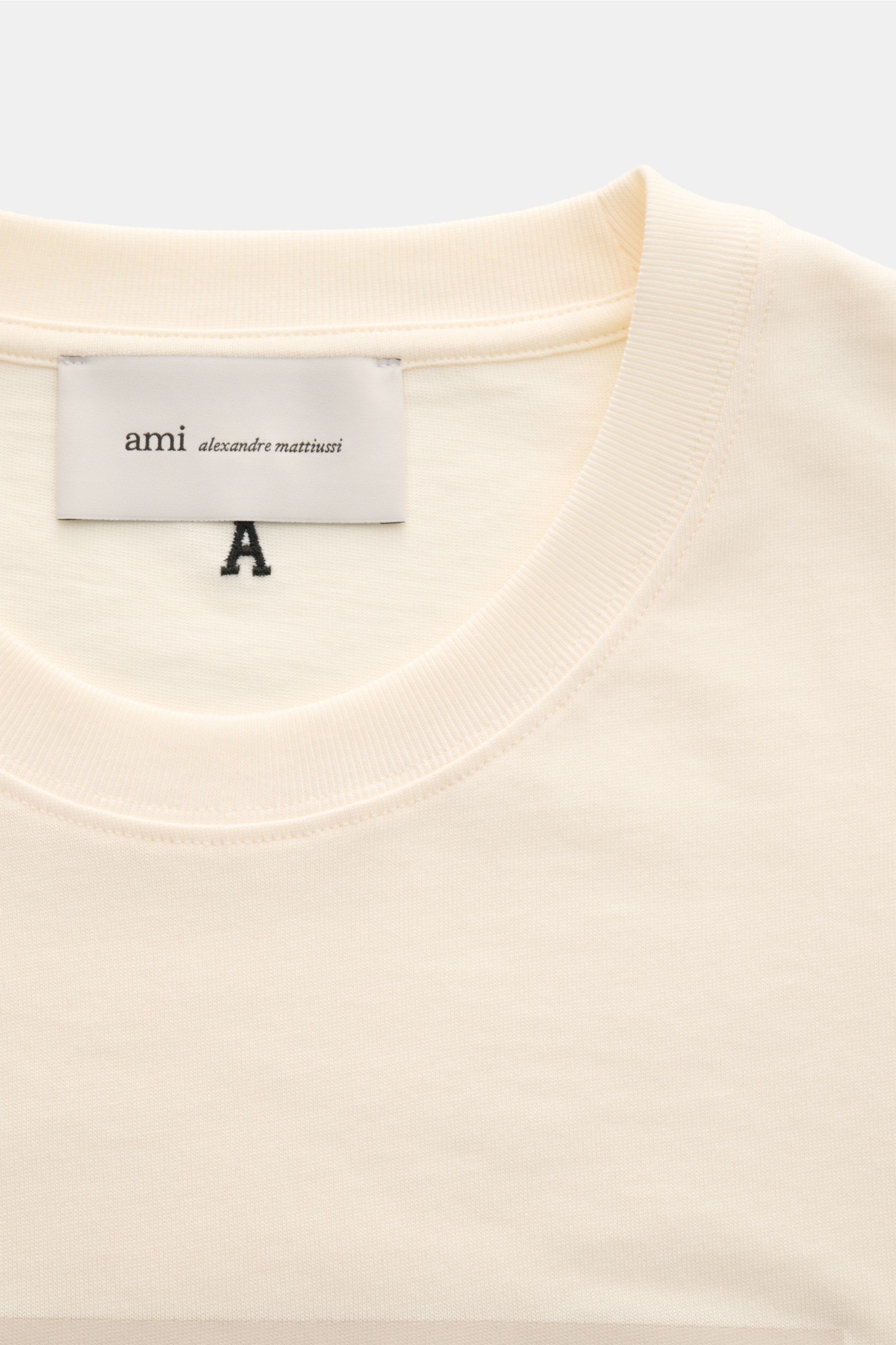 Ami Paris Rundhals-T-Shirt creme aus reiner Baumwolle mit weichem Griff, Regular Fit, Rundhalsausschnitt, geflocktem AMI PARIS-Schriftzug, Detailansicht von oben.
