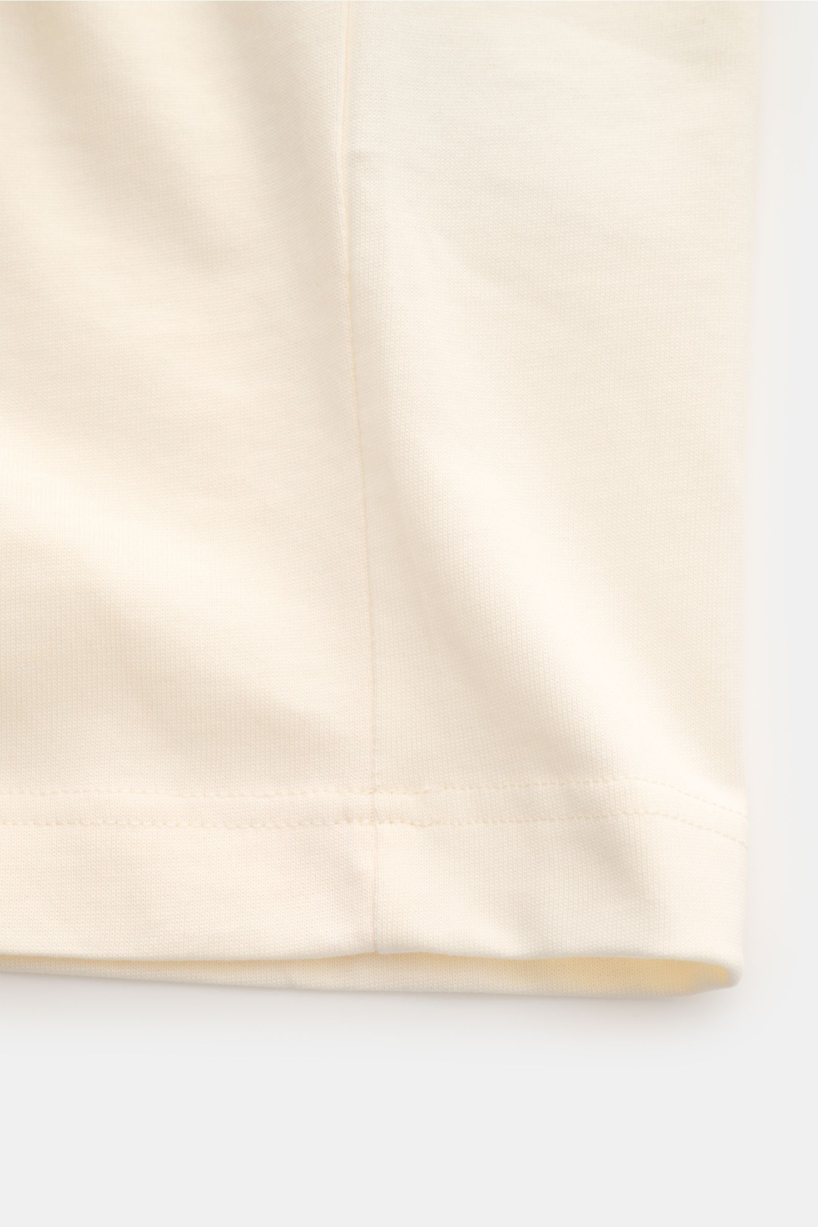 Ami Paris Rundhals-T-Shirt creme, Detailaufnahme vom Saum, Jersey aus reiner Baumwolle, weicher Griff, Regular Fit, geflockter Schriftzug vorne, Logo-Stitching hinten.