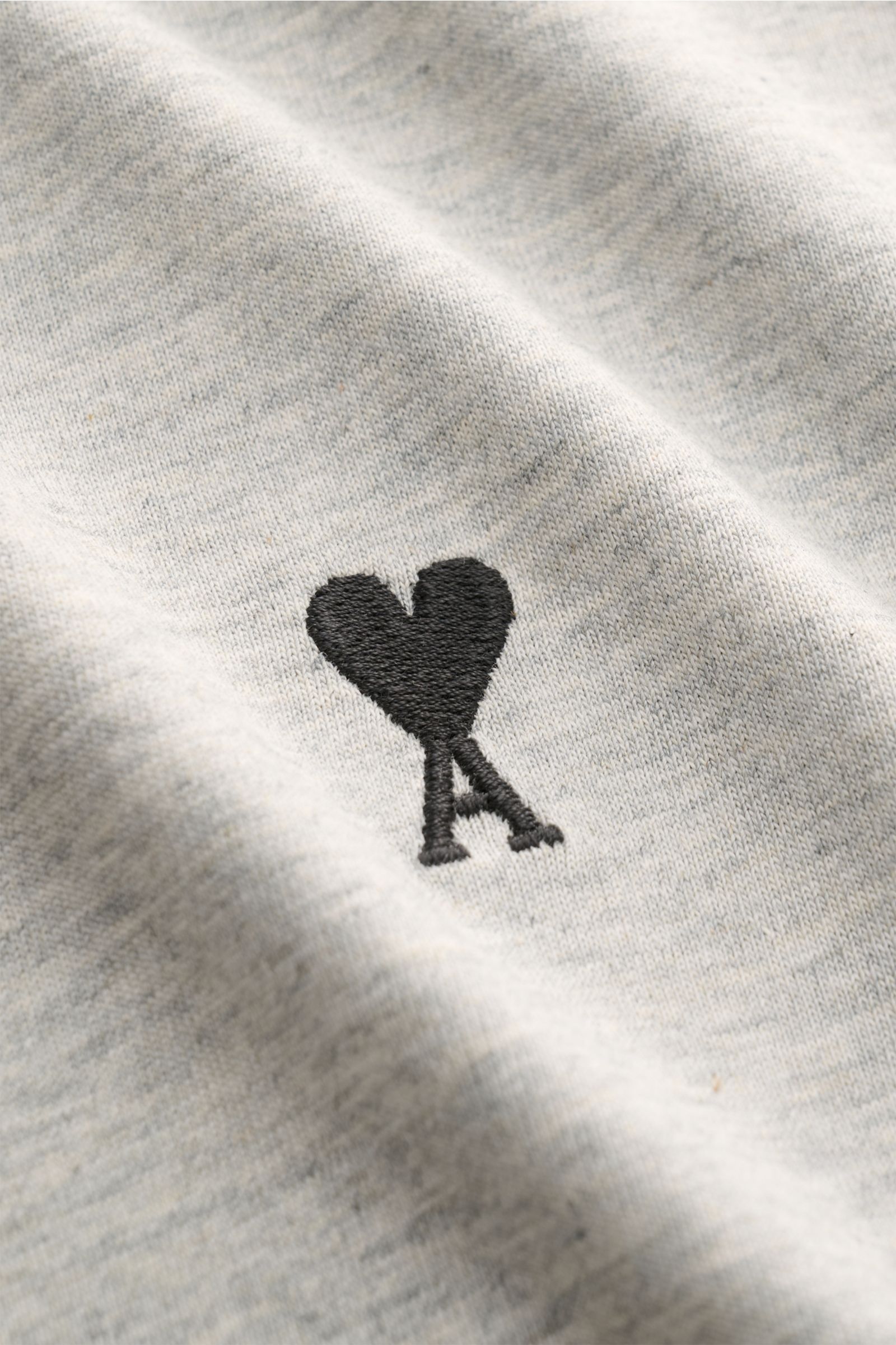 A close-up view of the Ami Paris Rundhals-T-Shirt grau meliert showing the black heart-stitching on soft grey melange cotton fabric. Klassisches Jersey-Basic vom französischen Label AMI PARIS: Dieses T-Shirt mit Rundhalsausschnitt ist aus reiner Baumwo