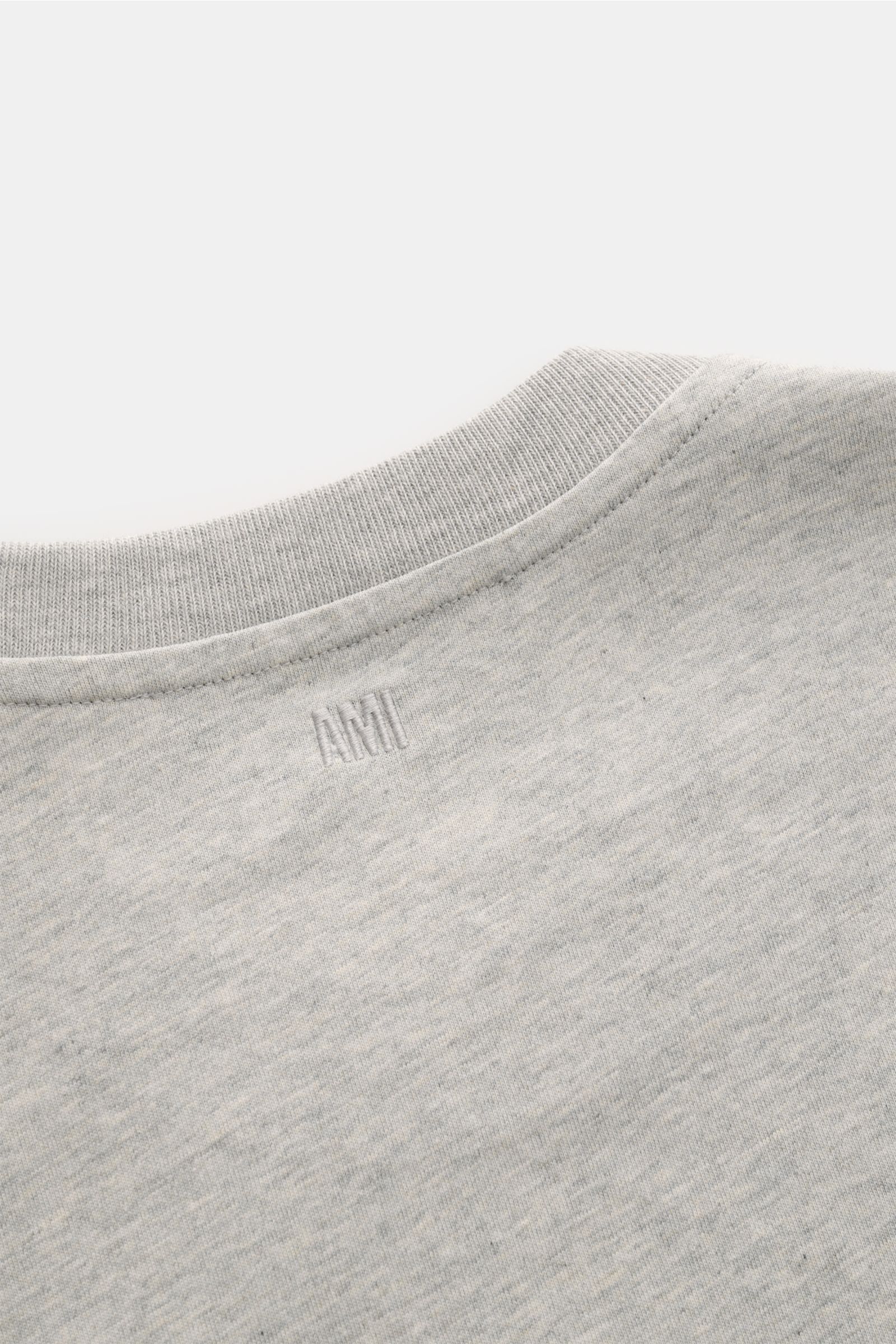 Close-up back view of the Ami Paris Rundhals-T-Shirt grau meliert, a classic slim fit grey melange cotton jersey tee with tonal AMI stitching on the back collar. 

Klassisches Jersey-Basic vom französischen Label AMI PARIS: Dieses T-Shirt mit Rundhalsa