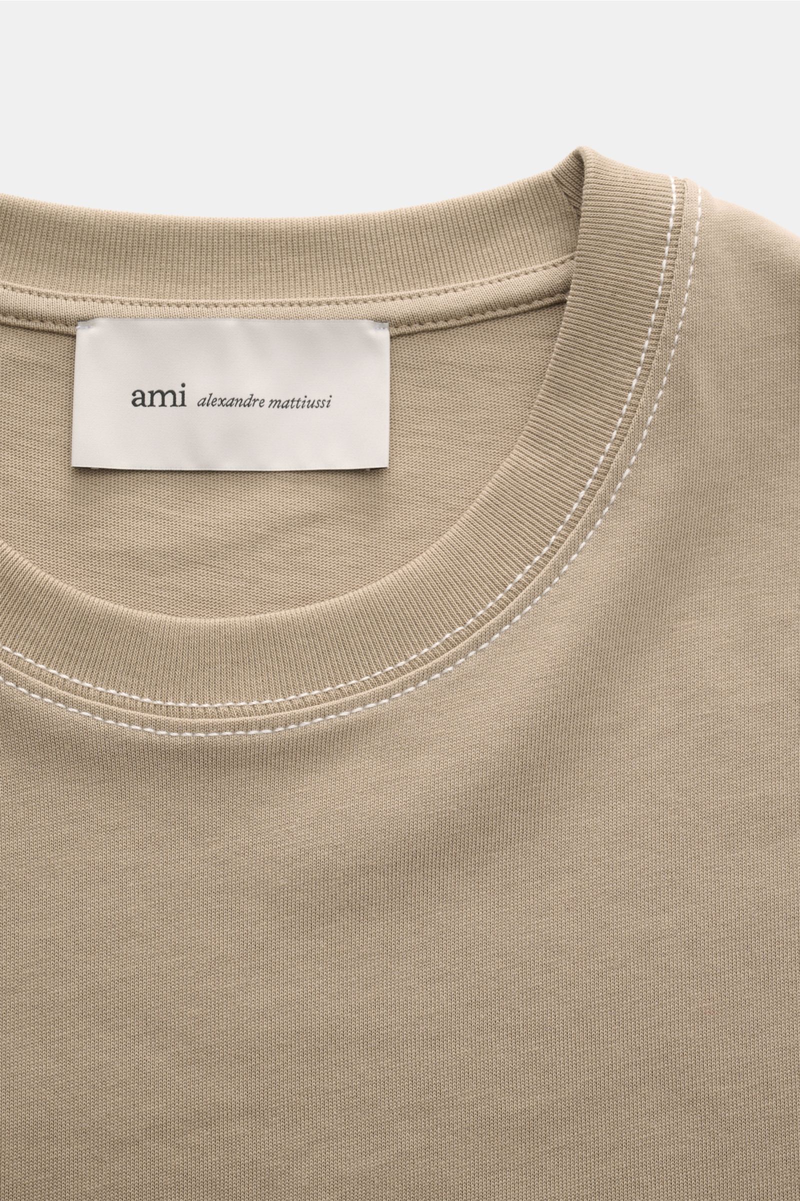 A close-up front view of the Ami Paris Rundhals-T-Shirt taupe, showing the round neckline, contrasting white topstitching, and the label inside the collar. Mit diesem T-Shirt von AMI PARIS können Sie coole Streetstyles kombinieren - die abgesteppten Nä