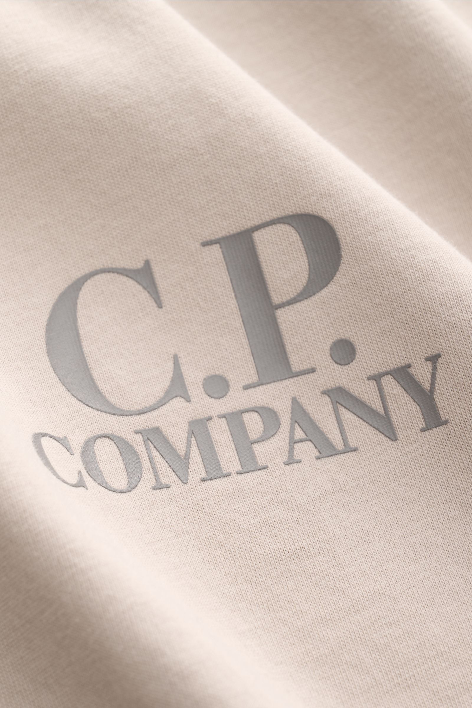 Nahaufnahme des beigen C.P. Company T-Shirts mit weichem Griff, Slim Fit und markantem Logo-Print auf Brust und Rücken.