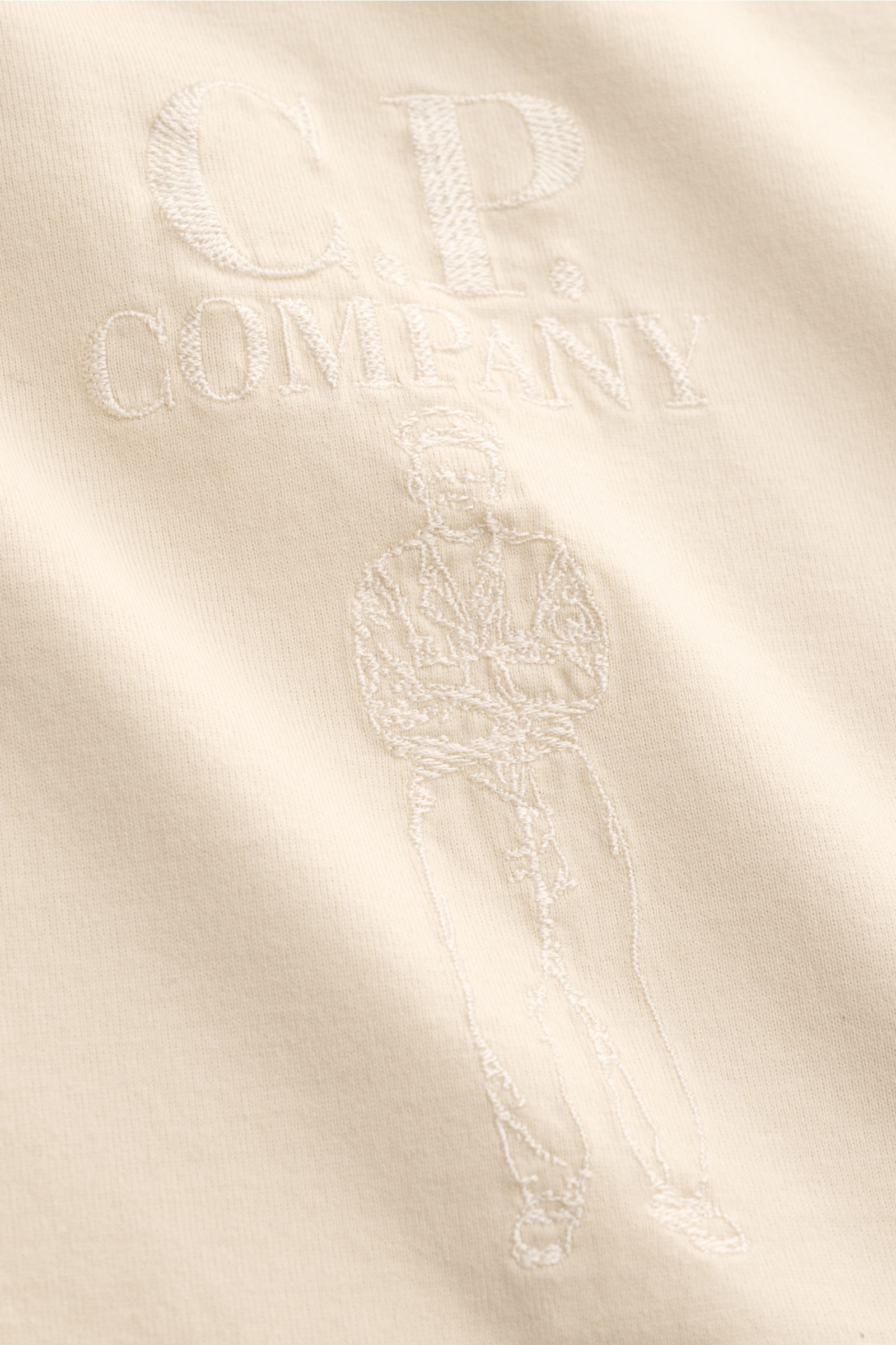 Nahaufnahme des sandfarbenen C.P. Company Rundhals-T-Shirts mit feinem Logo-Stitching und gestickter Figur, Jersey aus mercerisierter Baumwolle.
