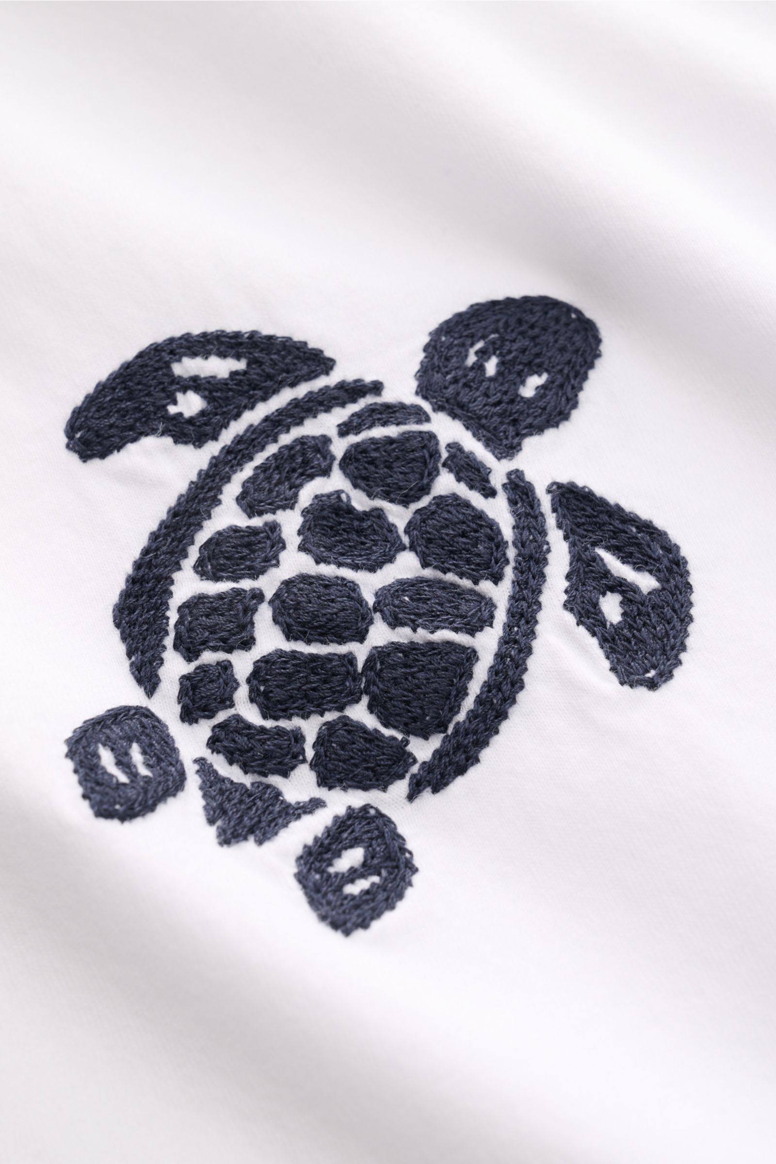 Nahaufnahme des aufwändigen Schildkröten-Stitchings auf dem weißen Vilebrequin Rundhals-T-Shirt 'Partisol' aus super soften Baumwoll-Jersey.