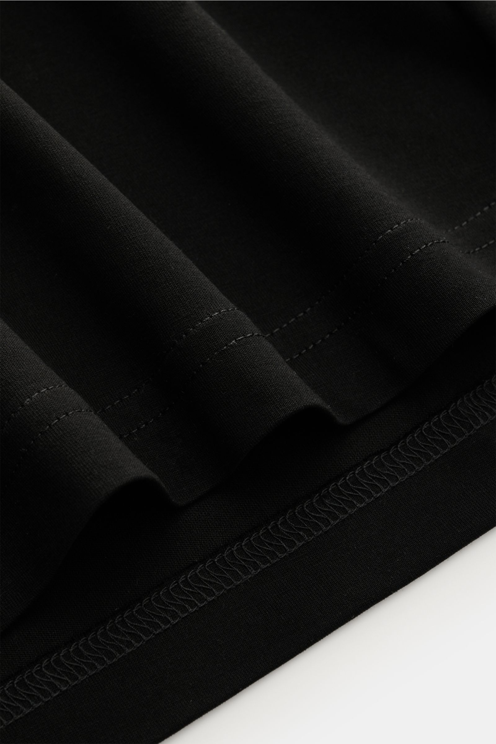 Close-up image of the hem of the Stefan Brandt Rundhals-T-Shirt 'Eli' schwarz, showing fine stitching and smooth black Pima cotton fabric from a side angle; Jersey in seiner feinsten Qualität: Mit seinem Expertenwissen über Materialien schafft STEFAN BRAN
