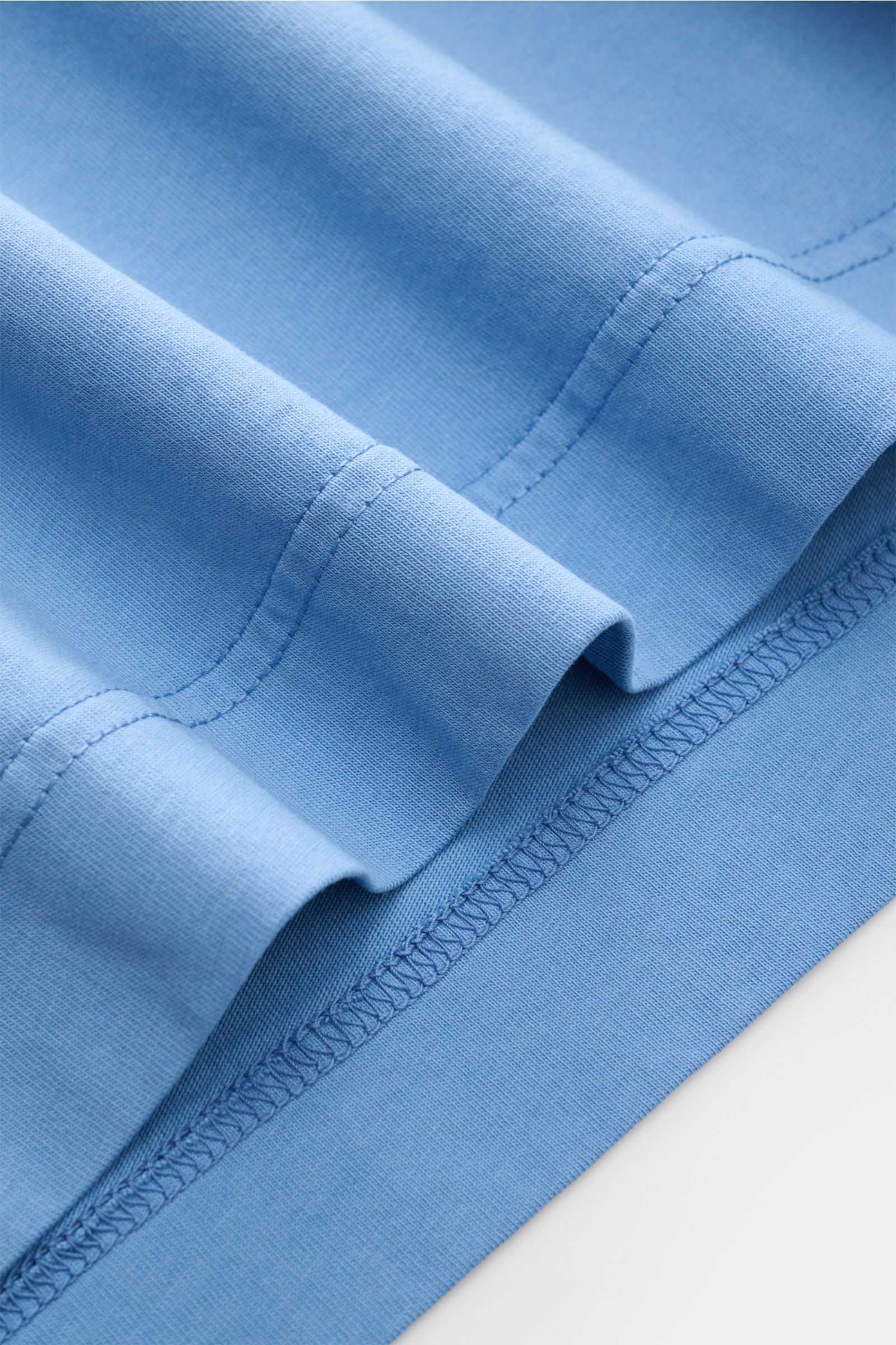 Nahaufnahme des B.F. Knitwear Rundhals-T-Shirts rauchblau von unten, reine Baumwolle, weicher Griff, Slim Fit, Rundhalsausschnitt, kurze Saumschlitze.