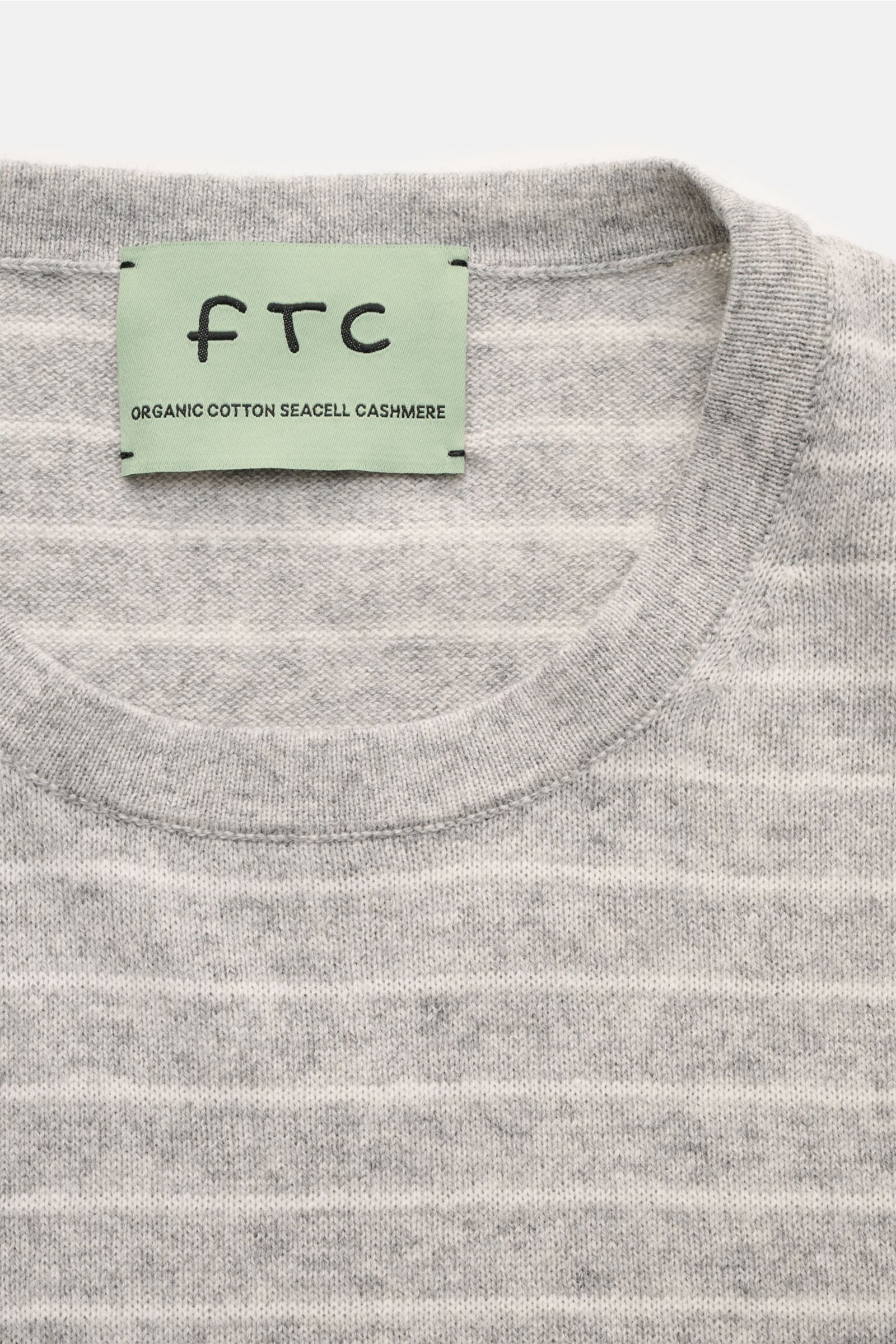 Nahaufnahme von oben auf den Rundhalsausschnitt und das Label des FTC Kurzarm-Rundhalspullover grau/weiß gestreift aus Cashmere-Baumwoll-SeaCell-Mix, feinem Strickbild, softem Material und rolliertem Saumabschluss im Regular Fit.