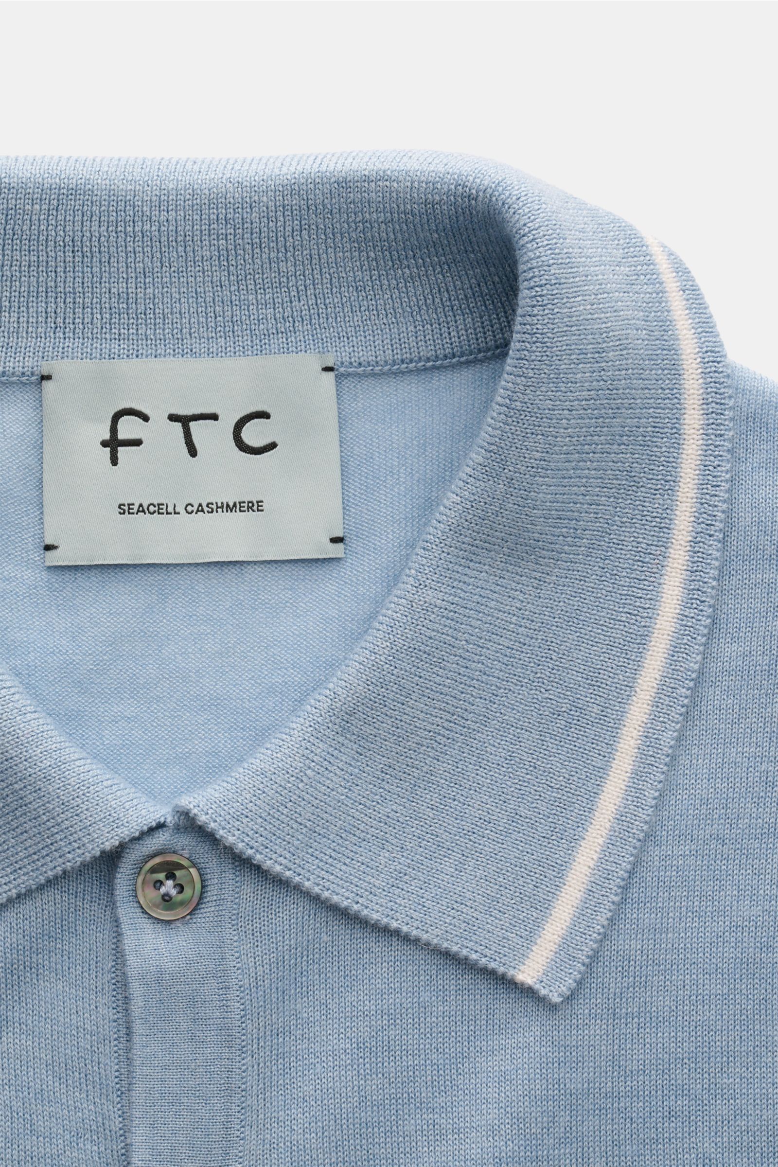 Nahaufnahme des FTC Kurzarm-Strickpolo hellblau mit klassischem Polokragen, drei Knöpfen, feinem Strickbild und schmalen Kontrastkanten aus nachhaltigem Cashmere-SeaCell-Mix.